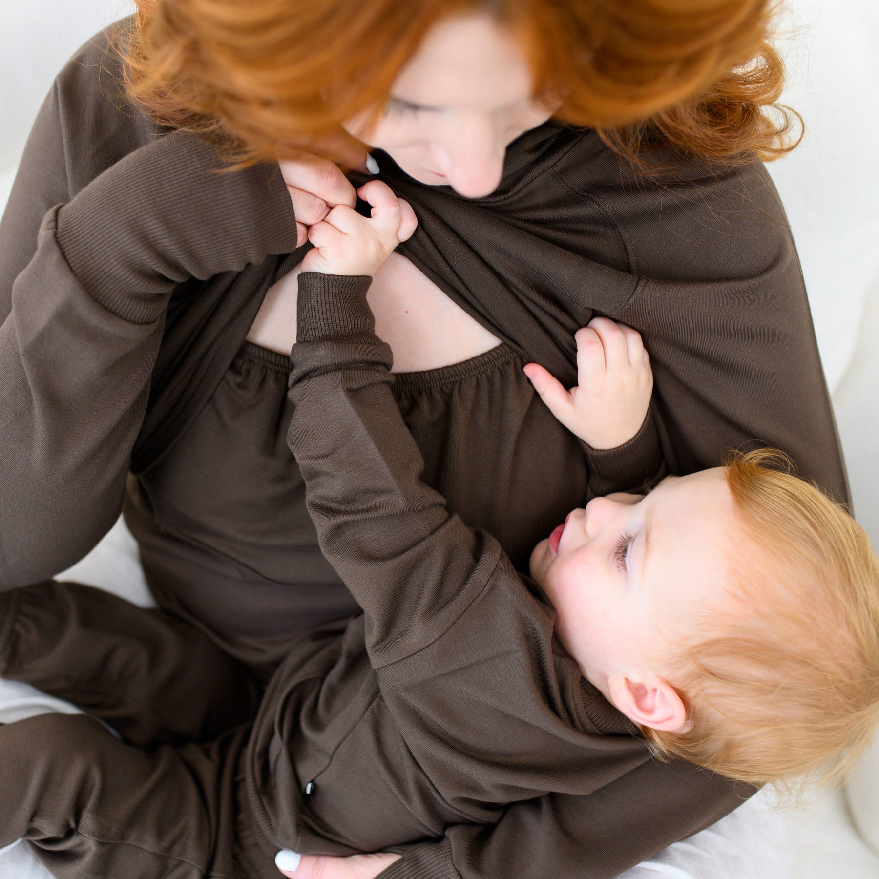 Mother wearing the Women's French Terry Nursing Hoodie in Espresso holding up the front fabric of the hoodie while holding her young infant