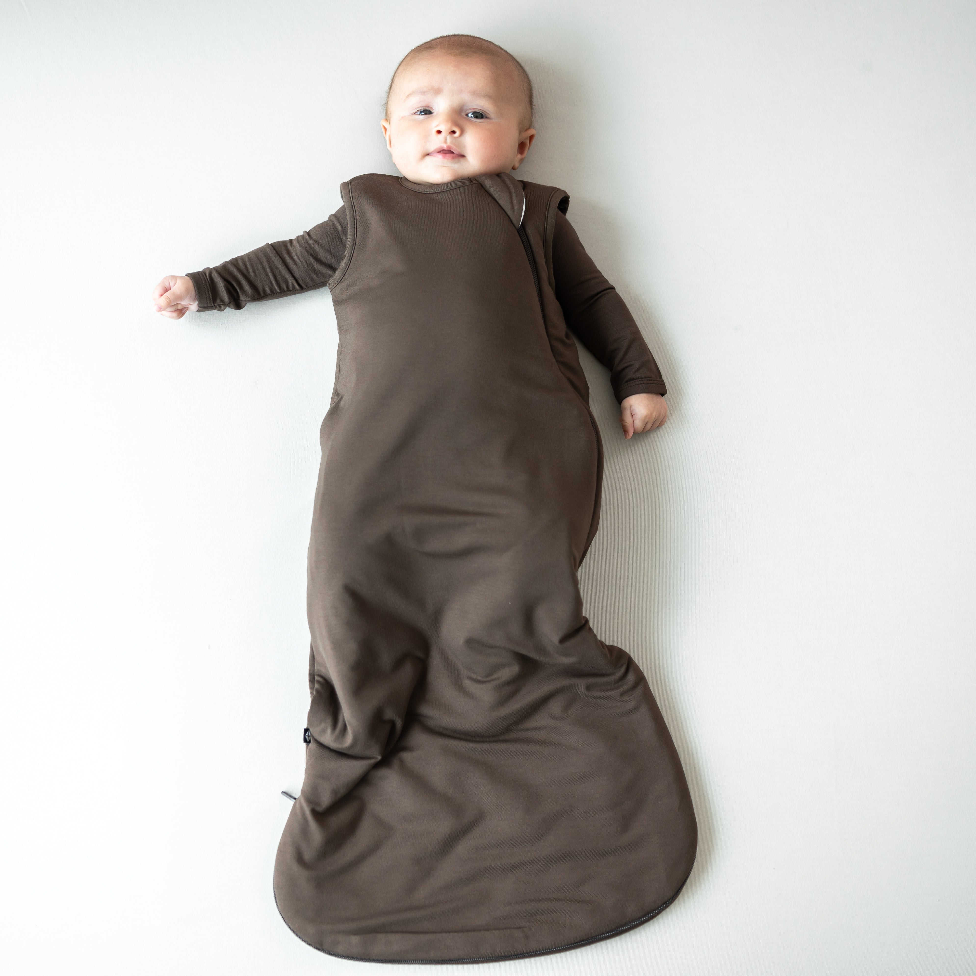 Infant laying down wearing the Sleep Bag in Espresso 1.0 with a matching long sleeve romper on underneath