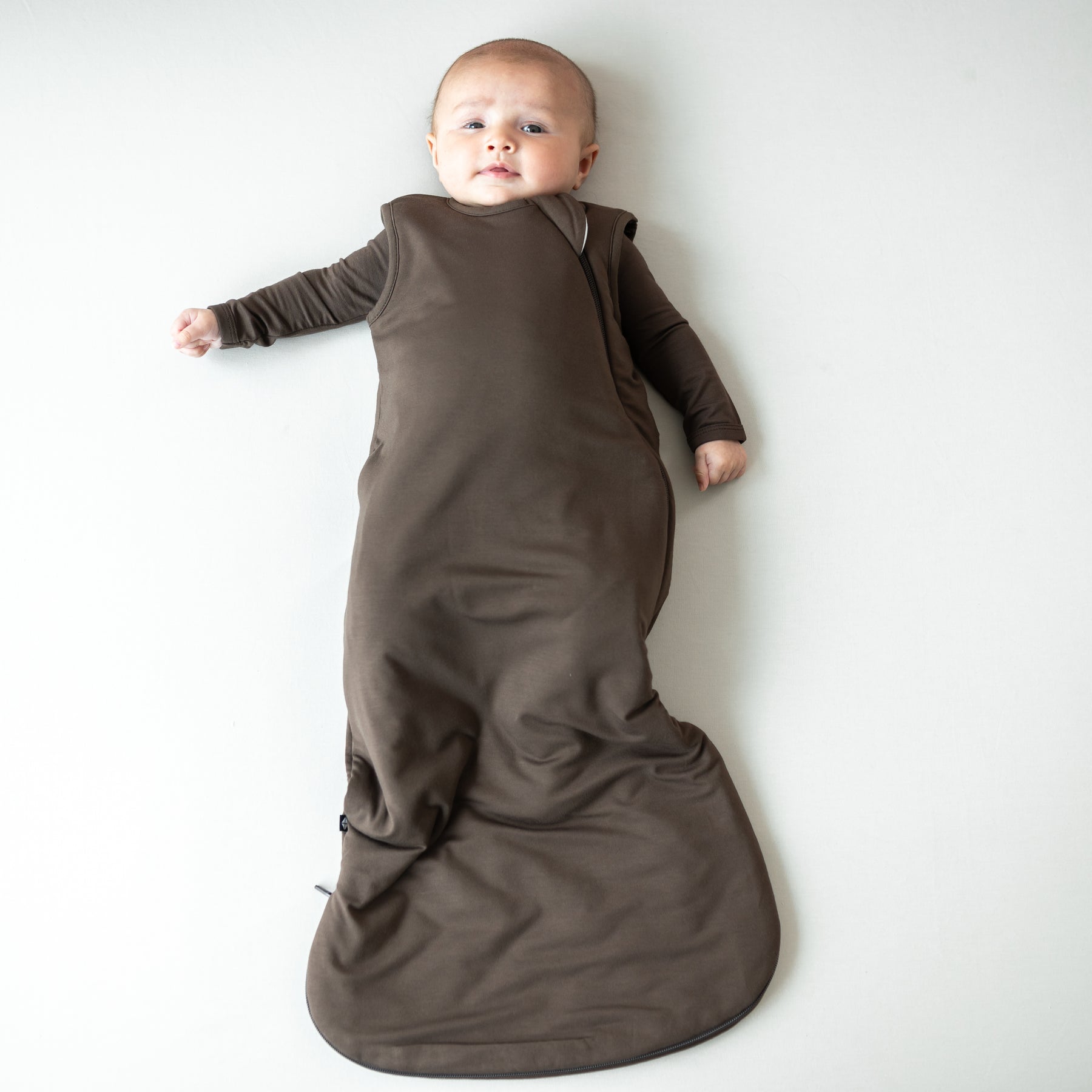 Infant laying down wearing the Sleep Bag in Espresso 1.0 with a matching long sleeve romper on underneath
