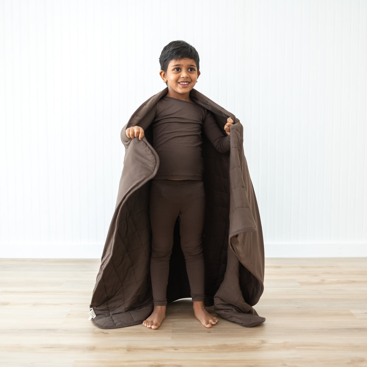 Boy model standing with the Toddler Blanket in Espresso 2.5 around him wearing matching toddler pajamas