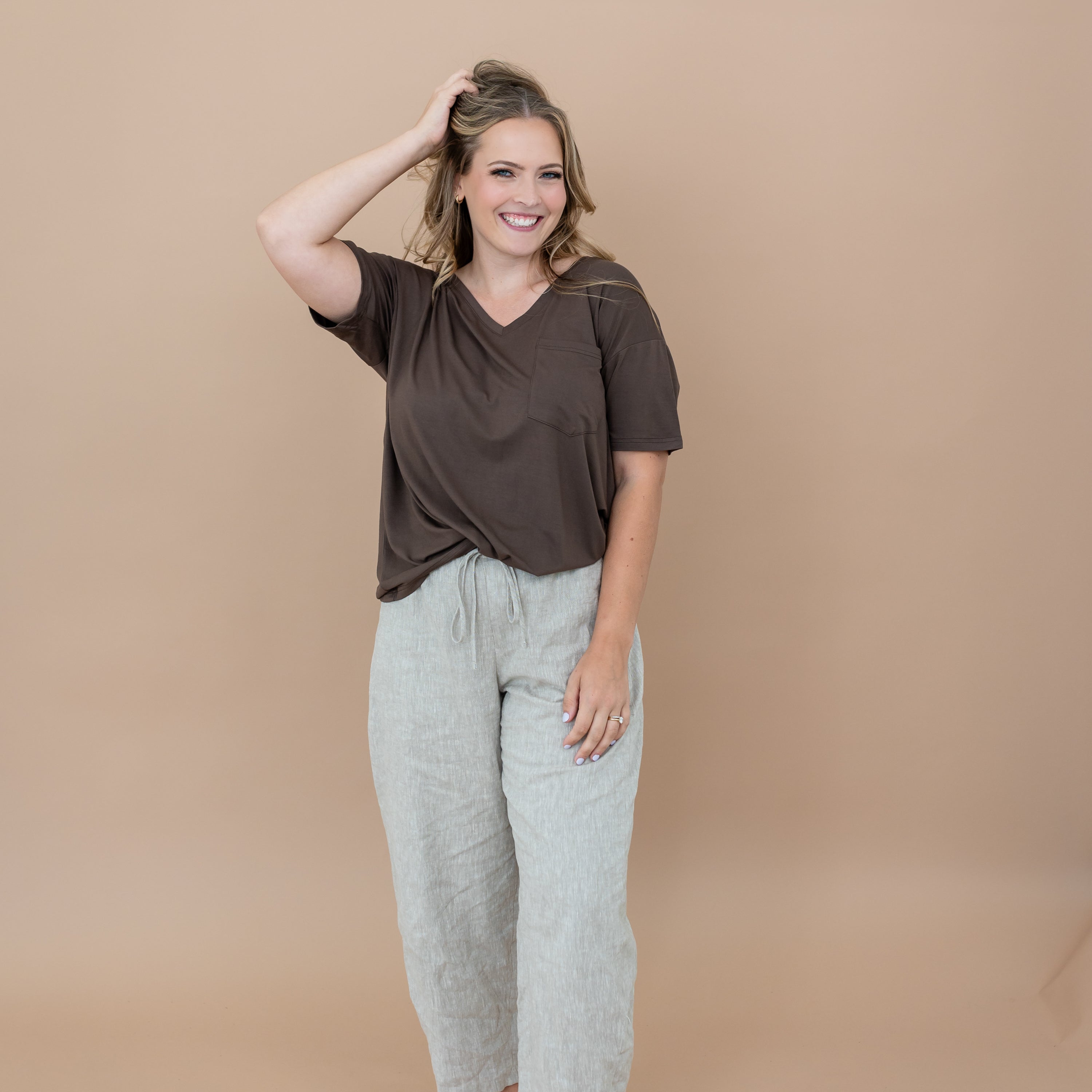 Female model standing with her one hand in her hair wearing the Women’s Relaxed Fit V-Neck in Espresso and linen pants