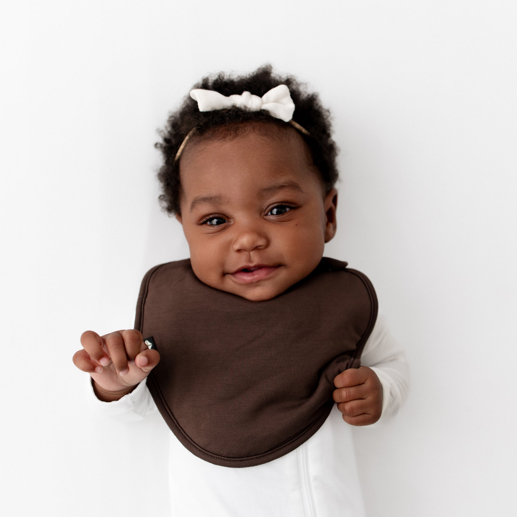 Infant girl wearing the Cushy Bib in Espresso paired with a Cloud Zippered footie