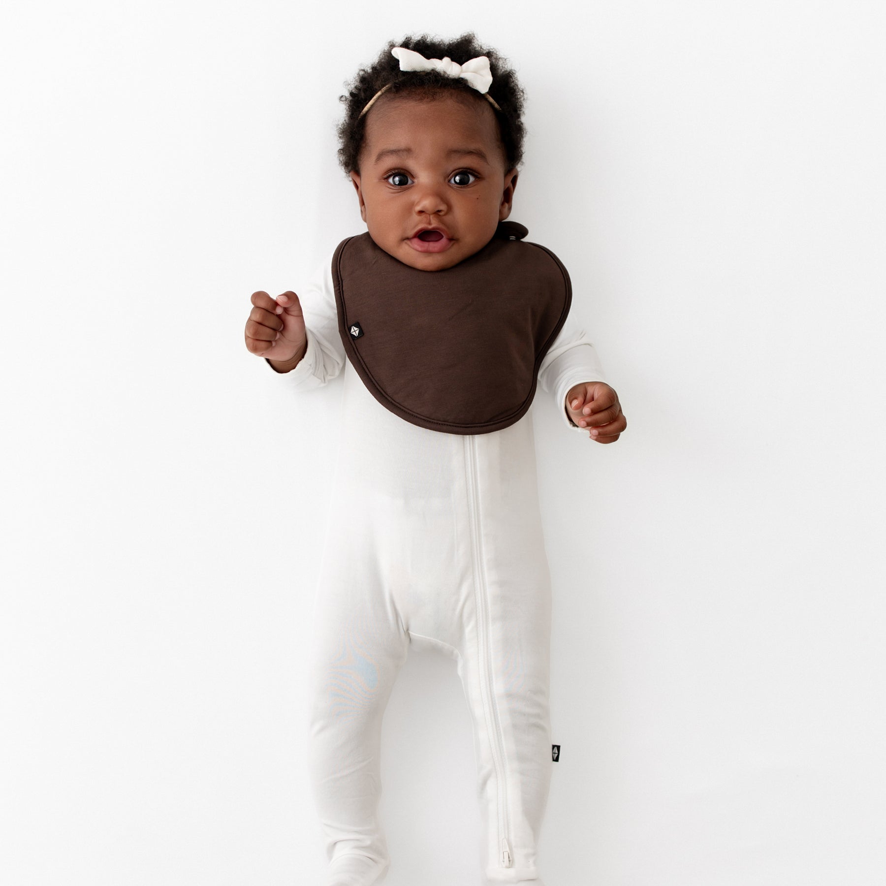 Infant girl wearing the Cushy Bib in Espresso paired with a Cloud Zippered footie