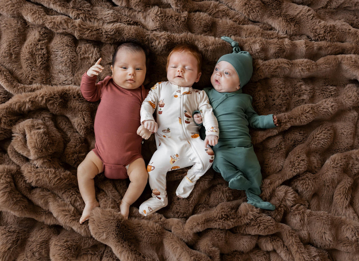 Group of 3 babies in fall layette laying on a brown fur blanket