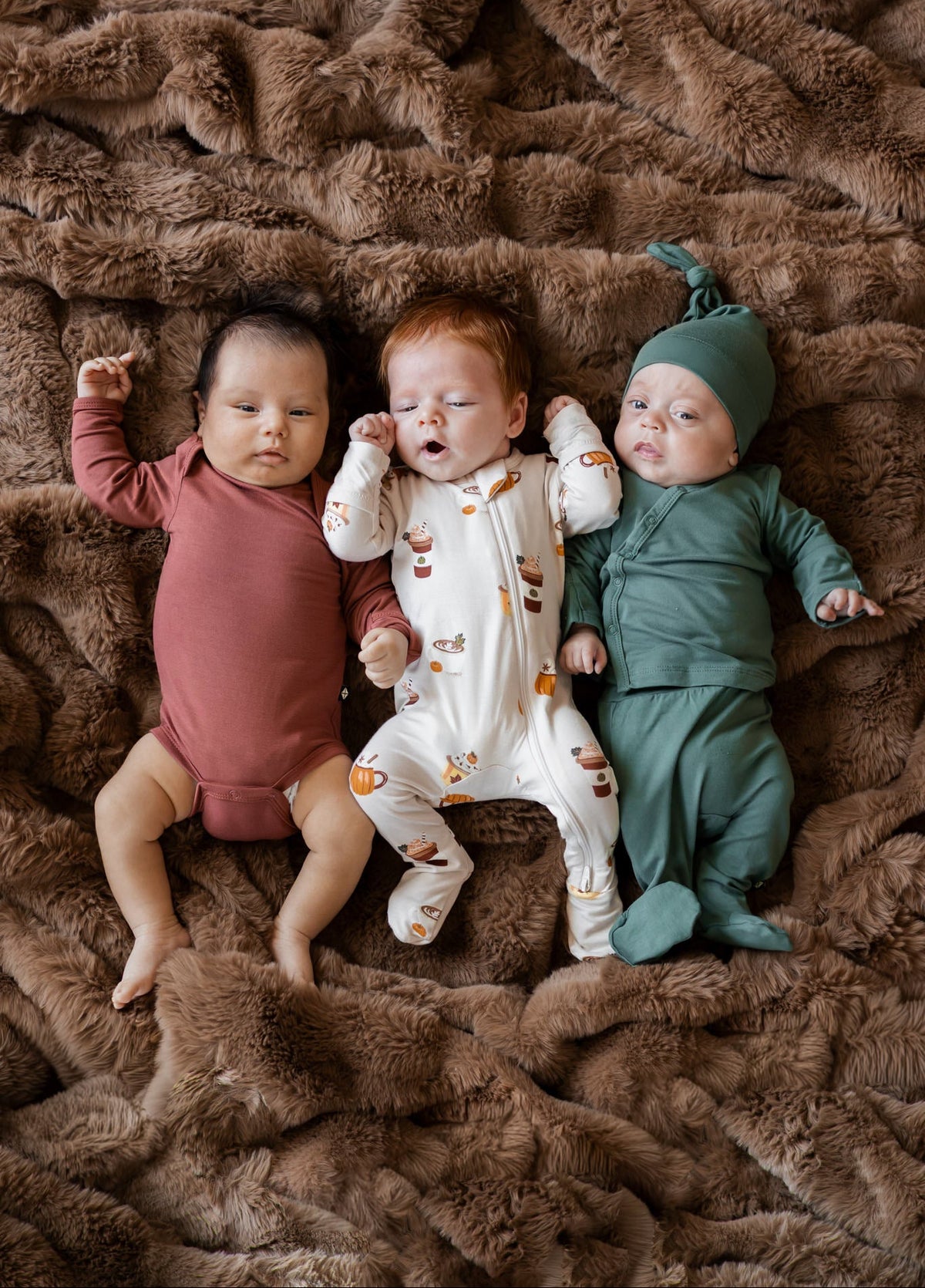 Group of 3 babies in fall layette laying on a brown fur blanket