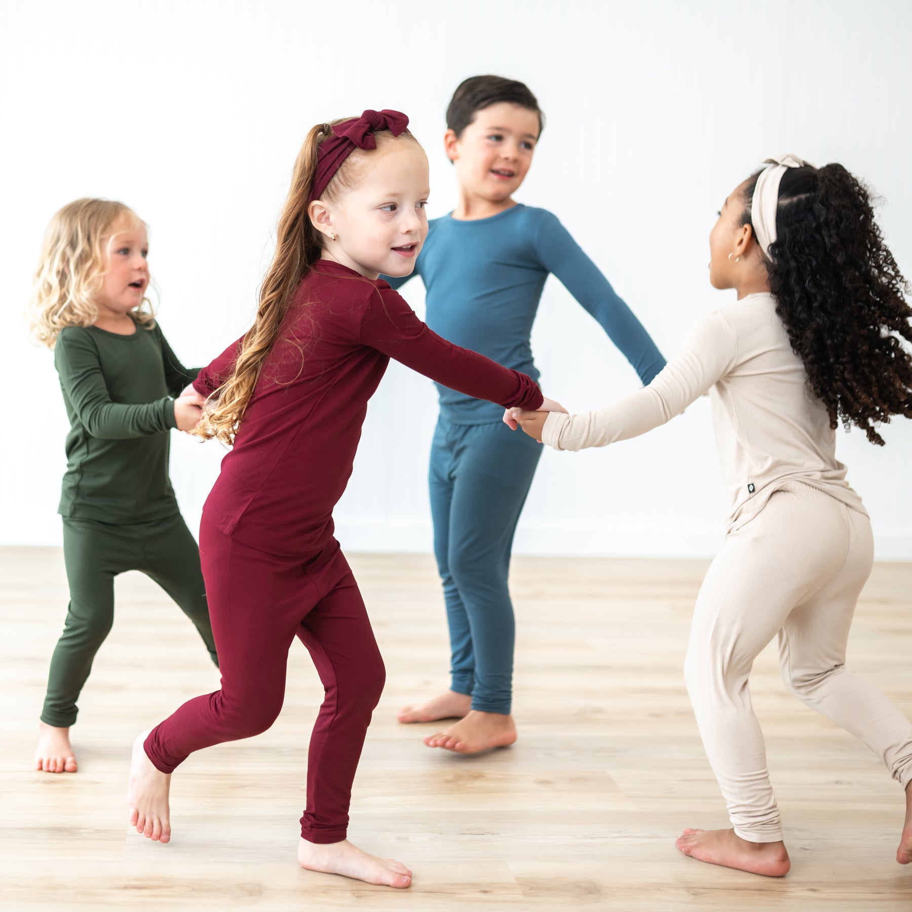 Kids holding hands going around in a circle wearing long sleeve toddler pajamas in Bisque, Atlantic, Fir and Burgundy