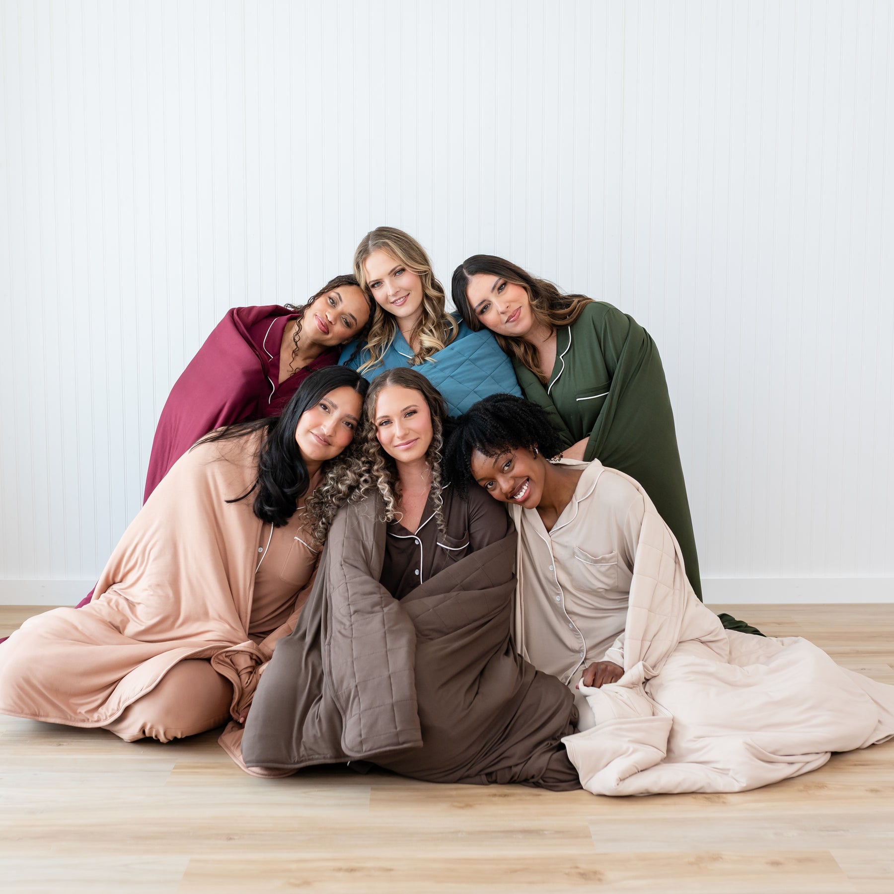 Group photo of six women wrapped in adult blankets wearing the corresponding women's pajama sets in fall colors