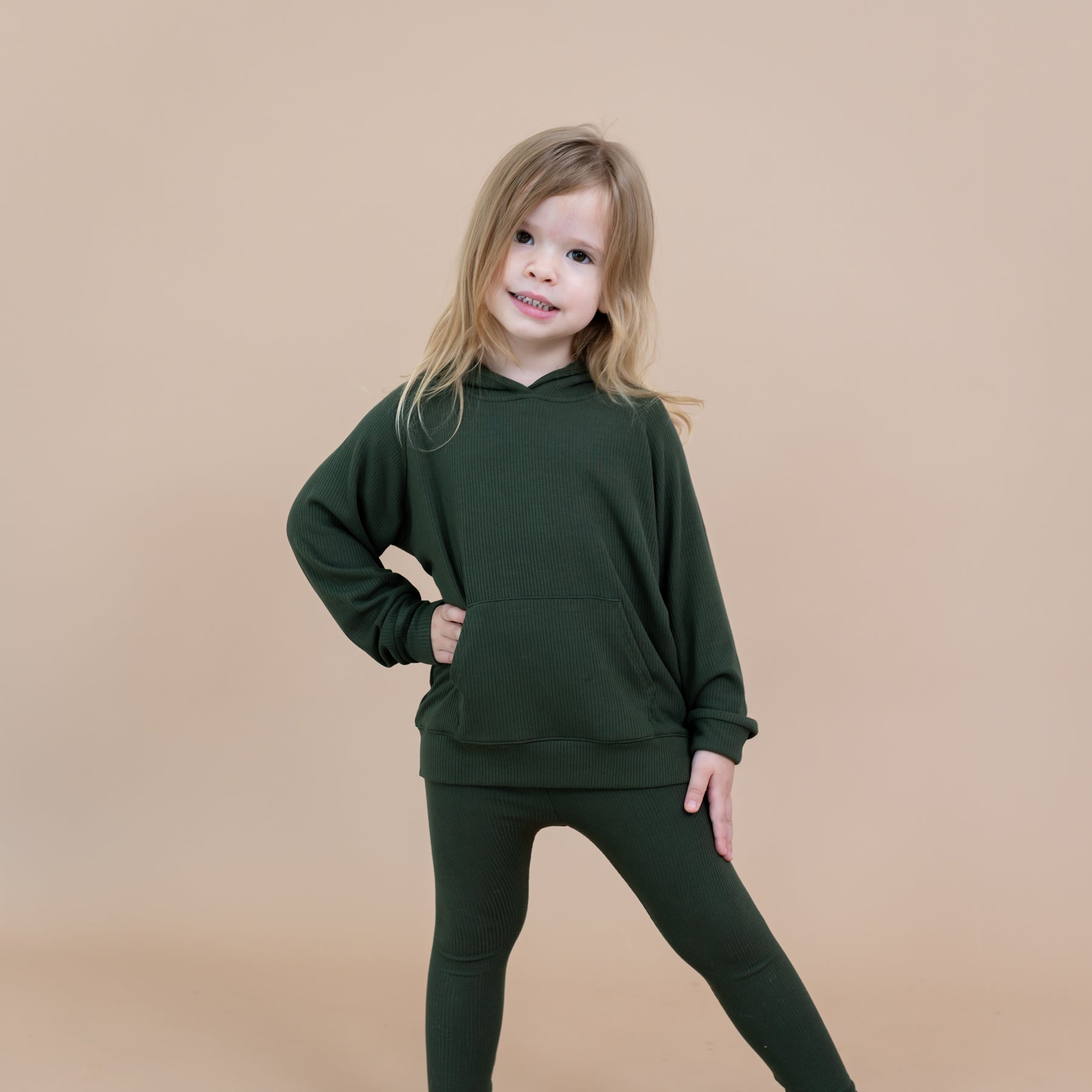 Young girl posing with one arm on her hip with the other on the top of her leg wearing the Ribbed Hoodie in Fir and matching ribbed leggings