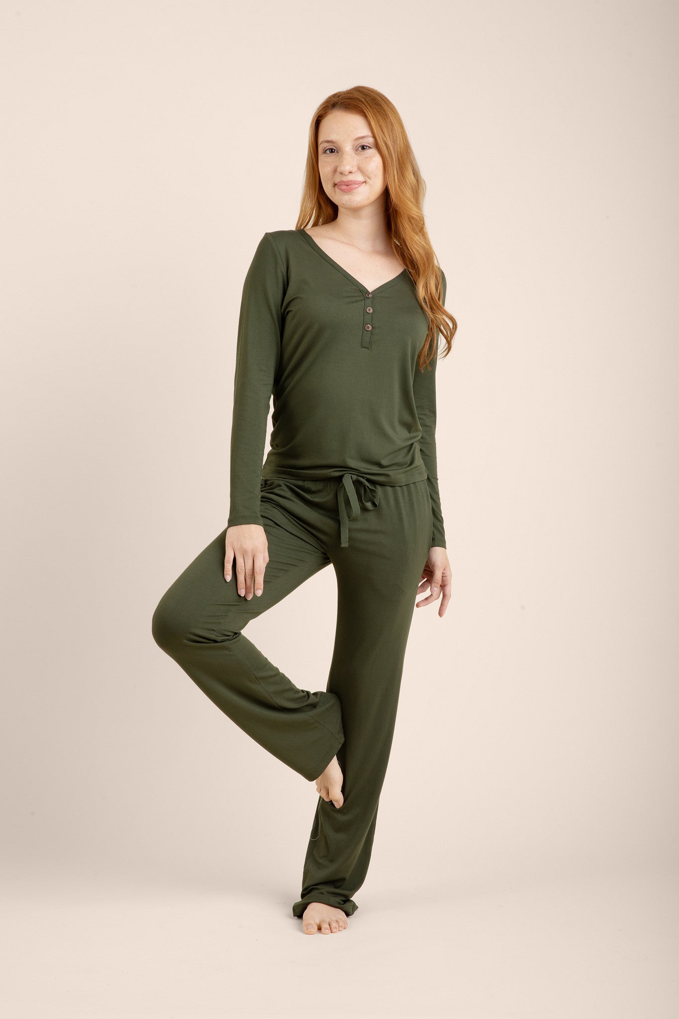 Female model standing on one leg wearing the Women's Long Sleeve Henley Tee in Fir with matching women's lounge pants