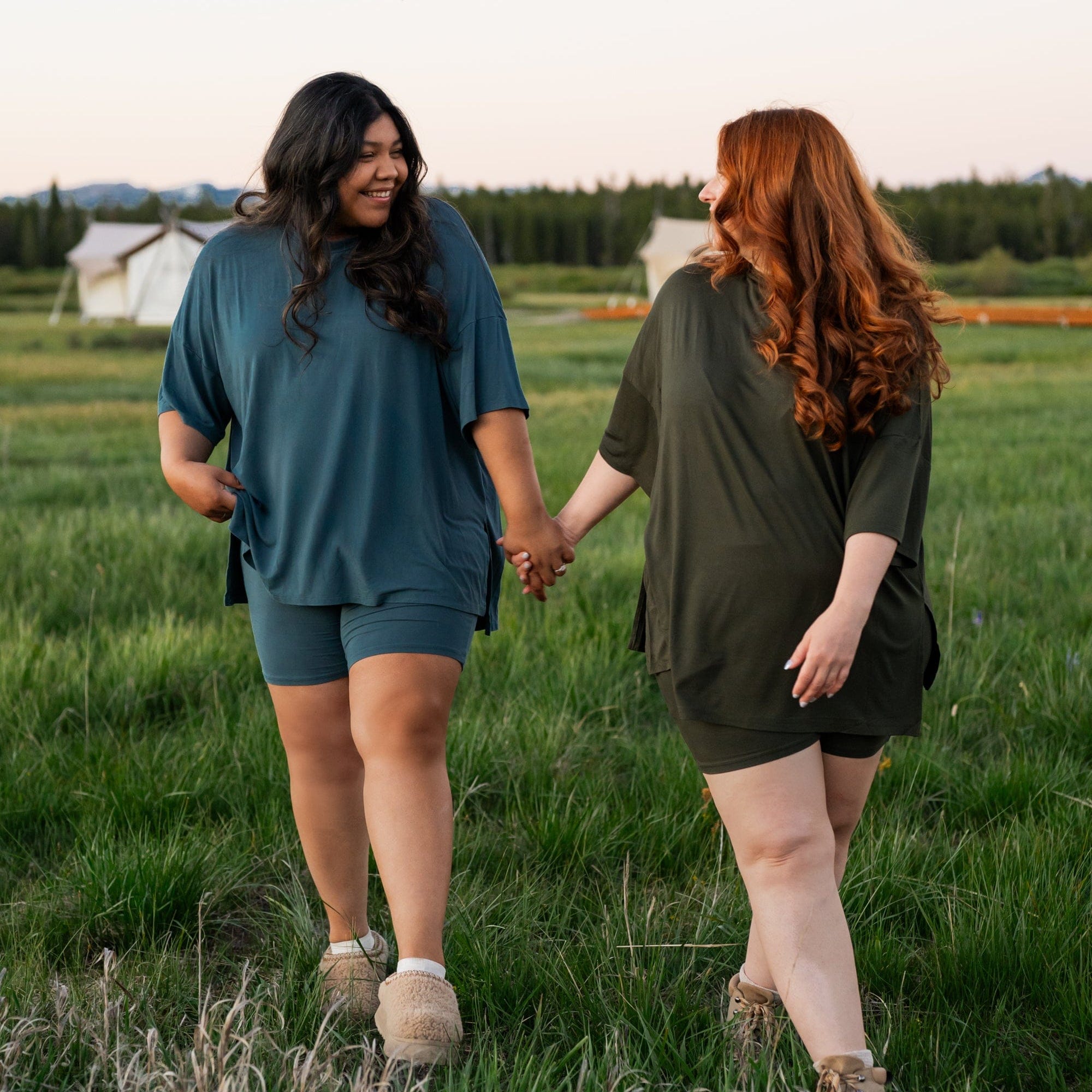 Two women holding hands and walking in a field during sunset wearing Kyte Baby bamboo biker short sets