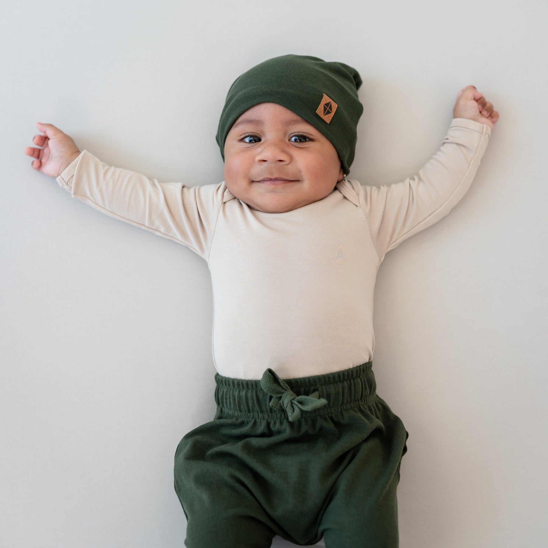 Infant wearing Bamboo Jersey Kids Beanie in Fir with green harem pants and Bisque long sleeve bodysuit
