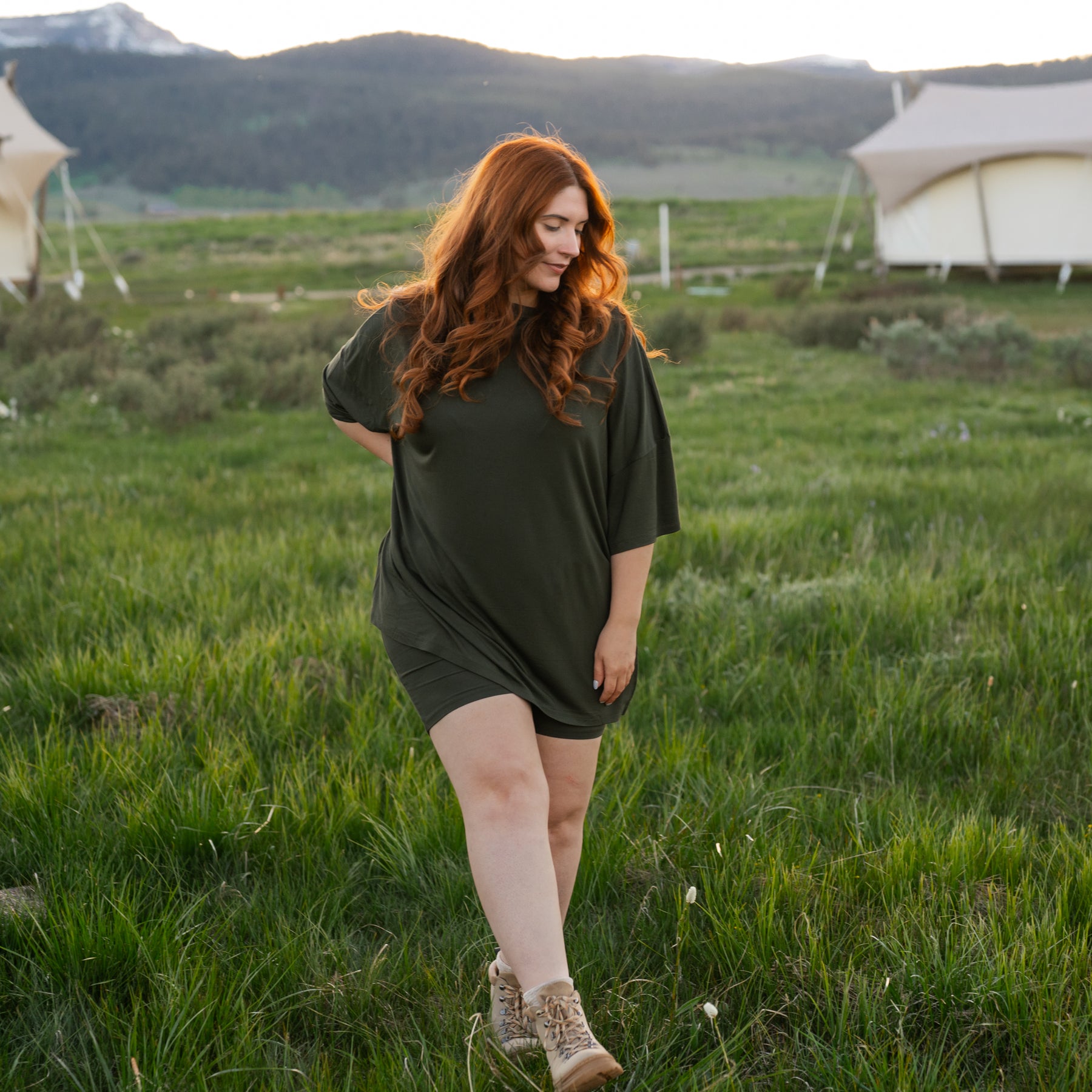 Woman with red hair wearing Women’s Biker Short Set in Fir walking in a grassy field with tents in the background