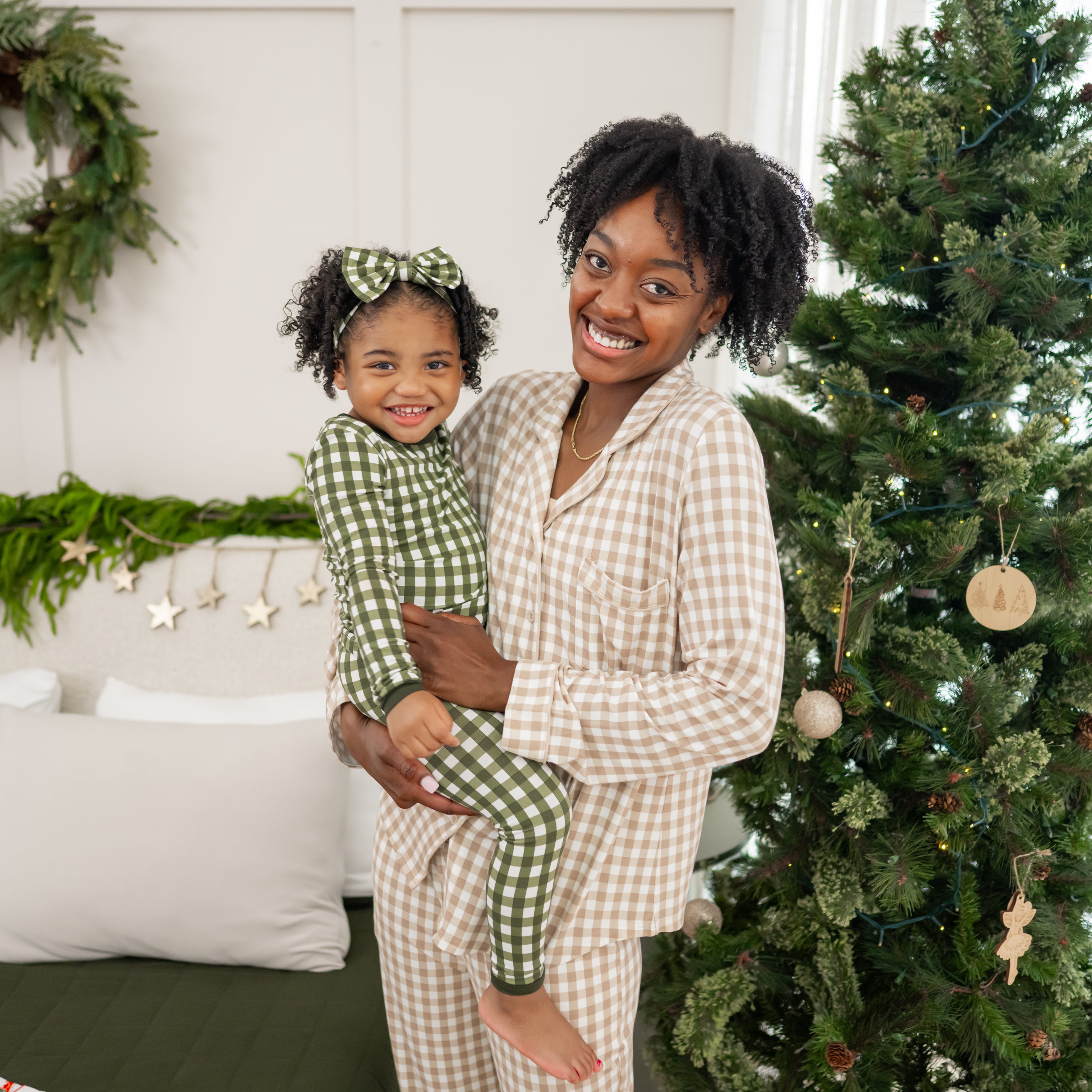 Mother wearing the Long-Sleeved Women's Pajama Set in Gingham Bisque holding daughter wearing the Long sleeve Toddler Pajama Set in Fir Gingham