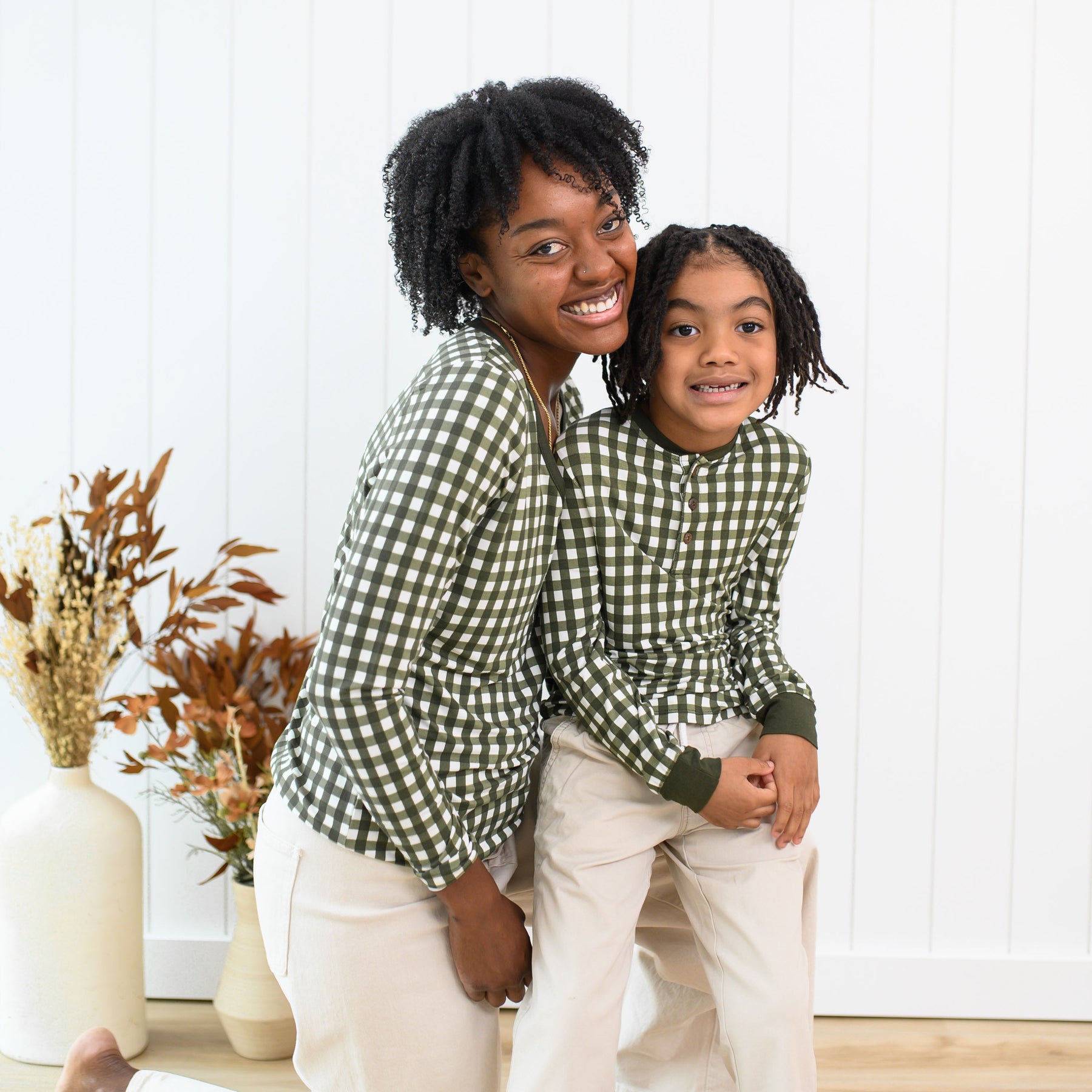 Mother kneeling on the ground with child sitting on her knee both wearing the Long Sleeve Henley Tee in Gingham Fir