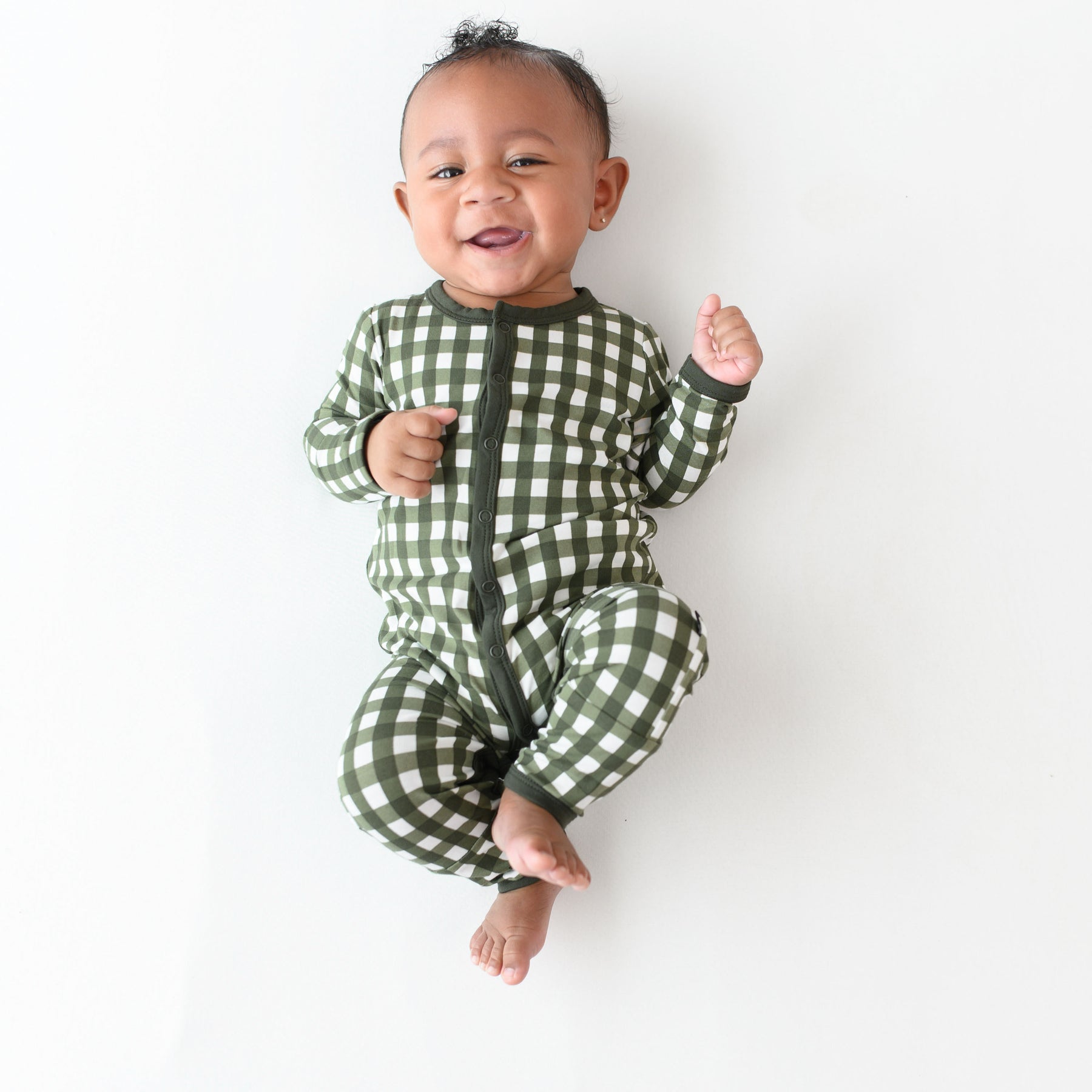 Smiling infant laying down wearing the Romper in Gingham Fir