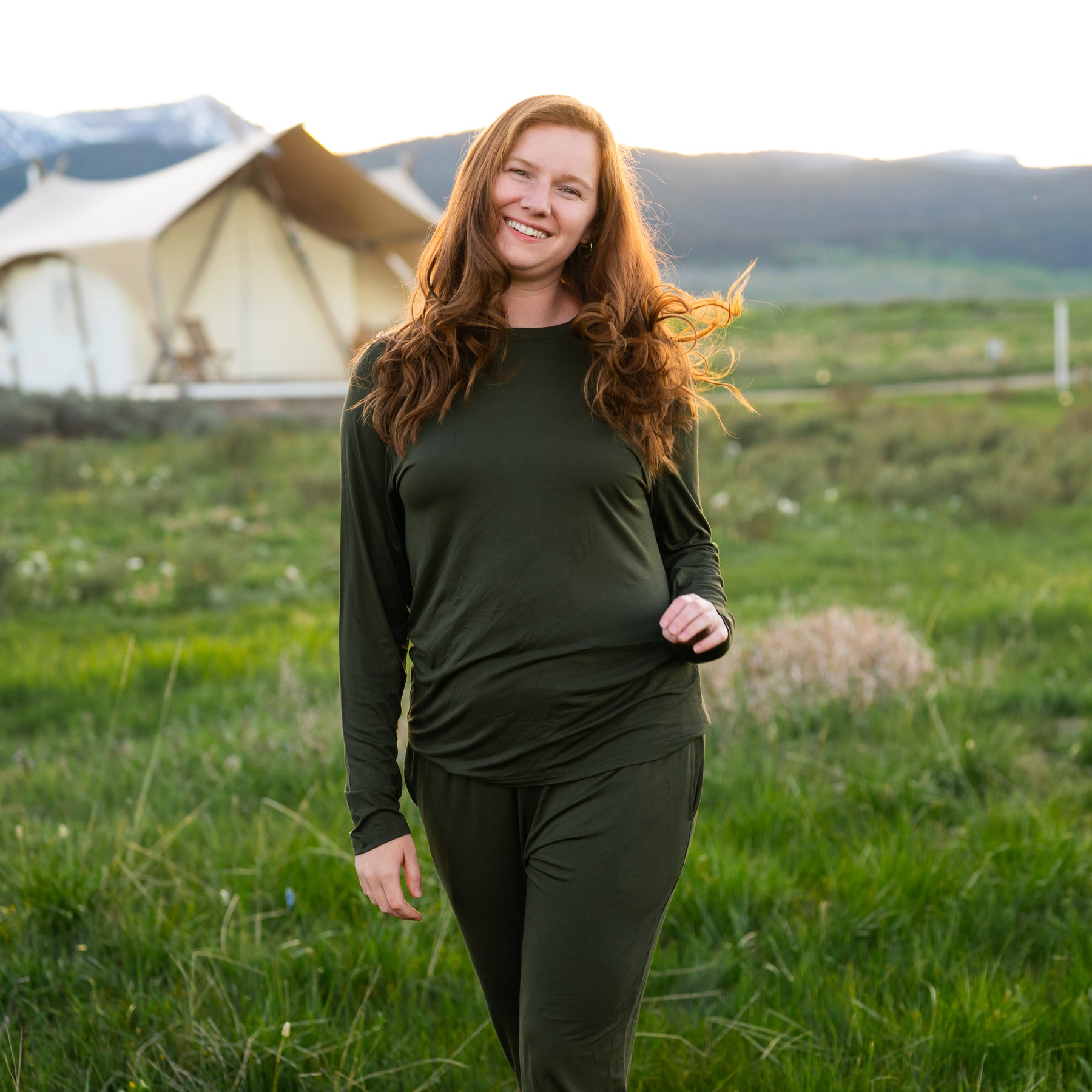 Woman Women's Jogger Pajama Set in Fir standing in a field with a tent and mountains in the background