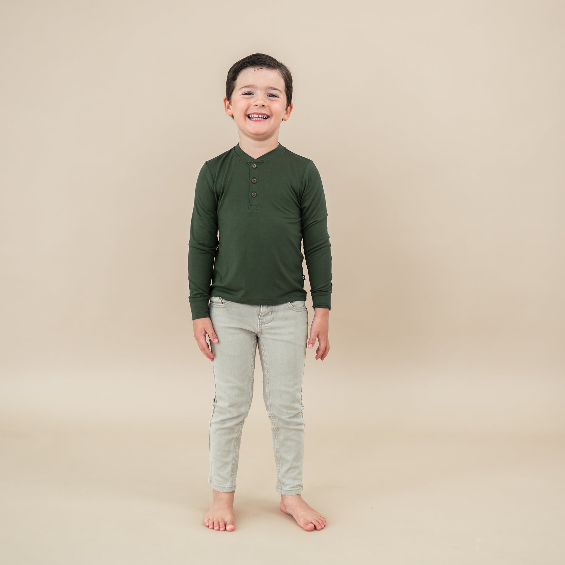 Child wearing Long Sleeve Toddler Henley Tee in Fir on tan backdrop