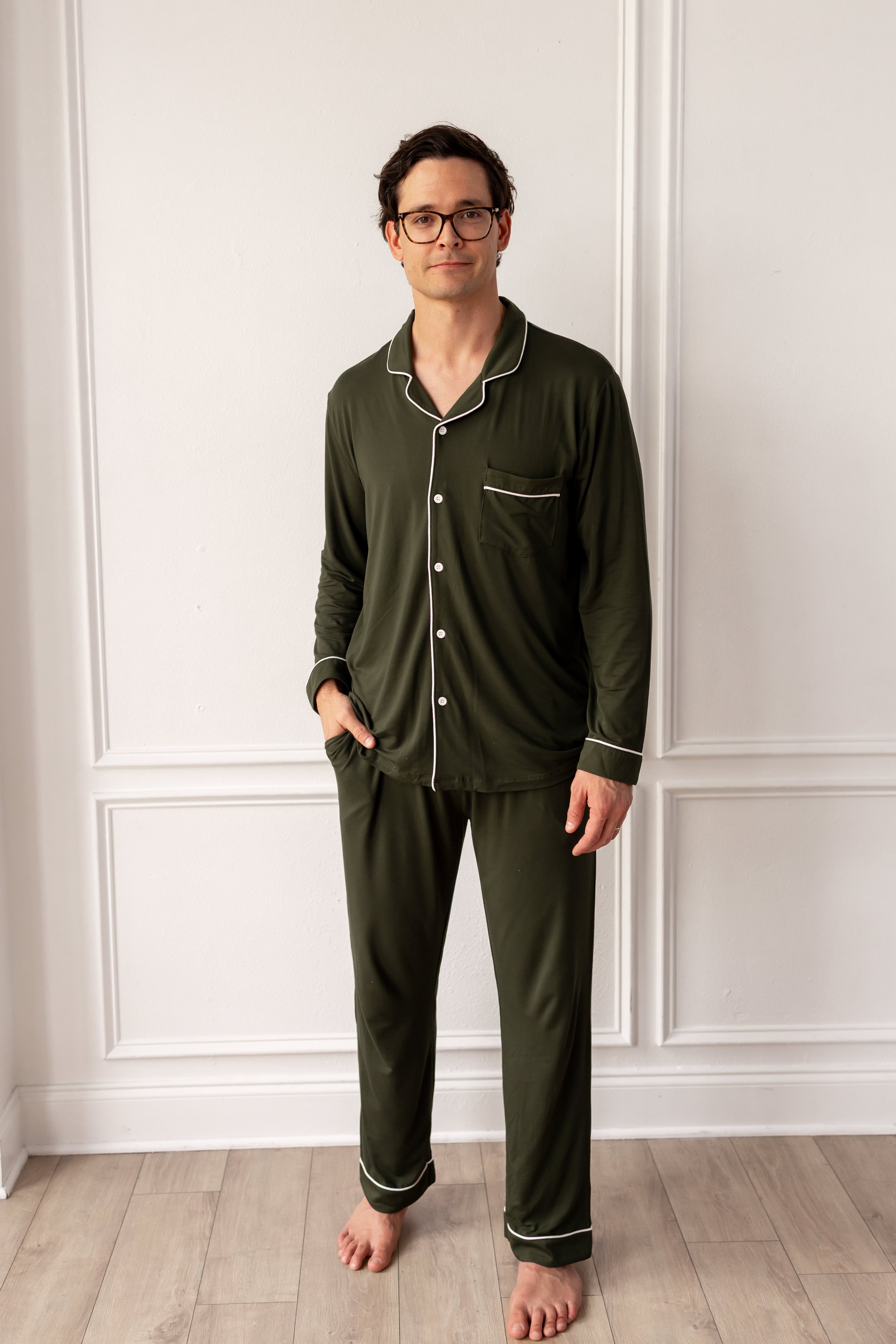 Man wearing green pajamas standing against a white paneled wall.