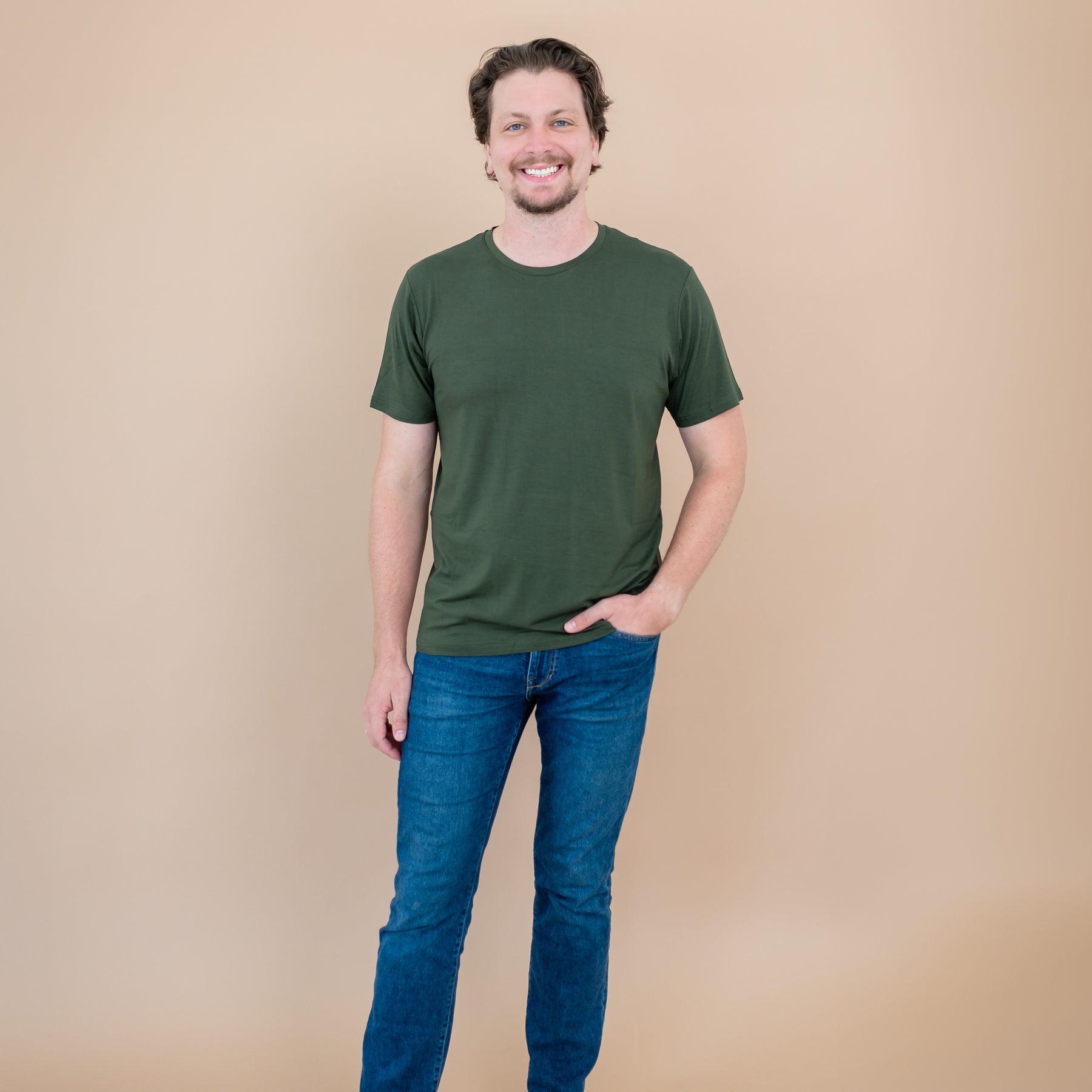 Man wearing a green t-shirt and blue jeans against a beige background