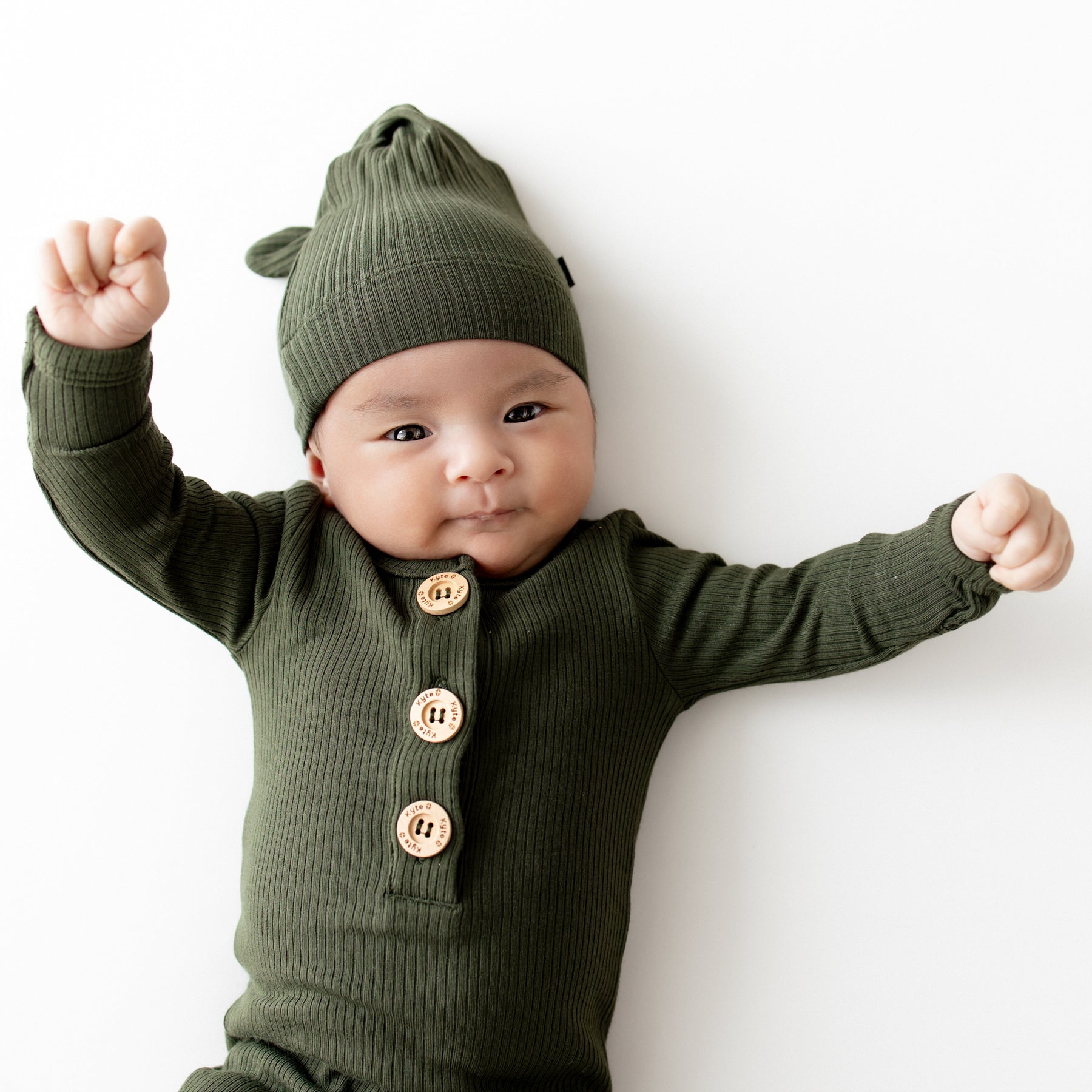 Close up of an infant wearing the Ribbed Knotted Gown with Hat Set in Fir with their arms in the air