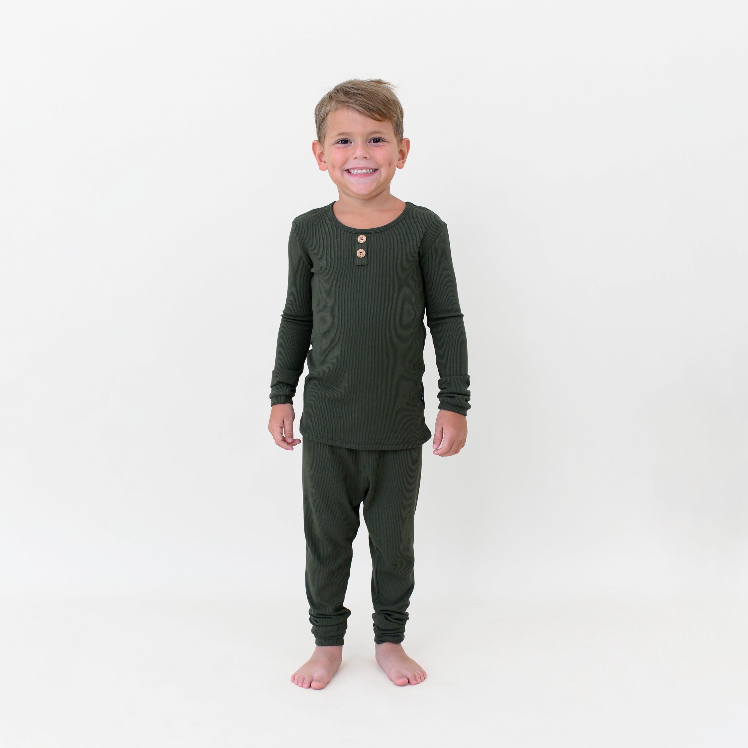 Smiling boy standing in front of a white colored background wearing the Ribbed Henley Set in Fir