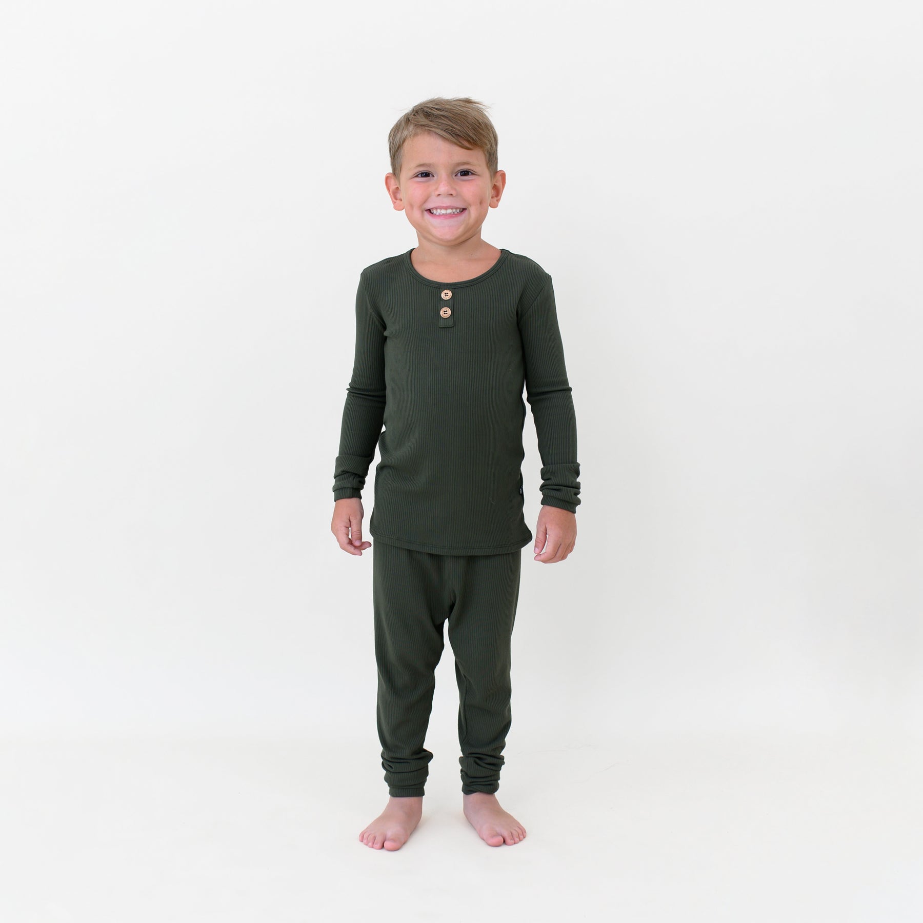 Smiling boy standing in front of a white colored background wearing the Ribbed Henley Set in Fir