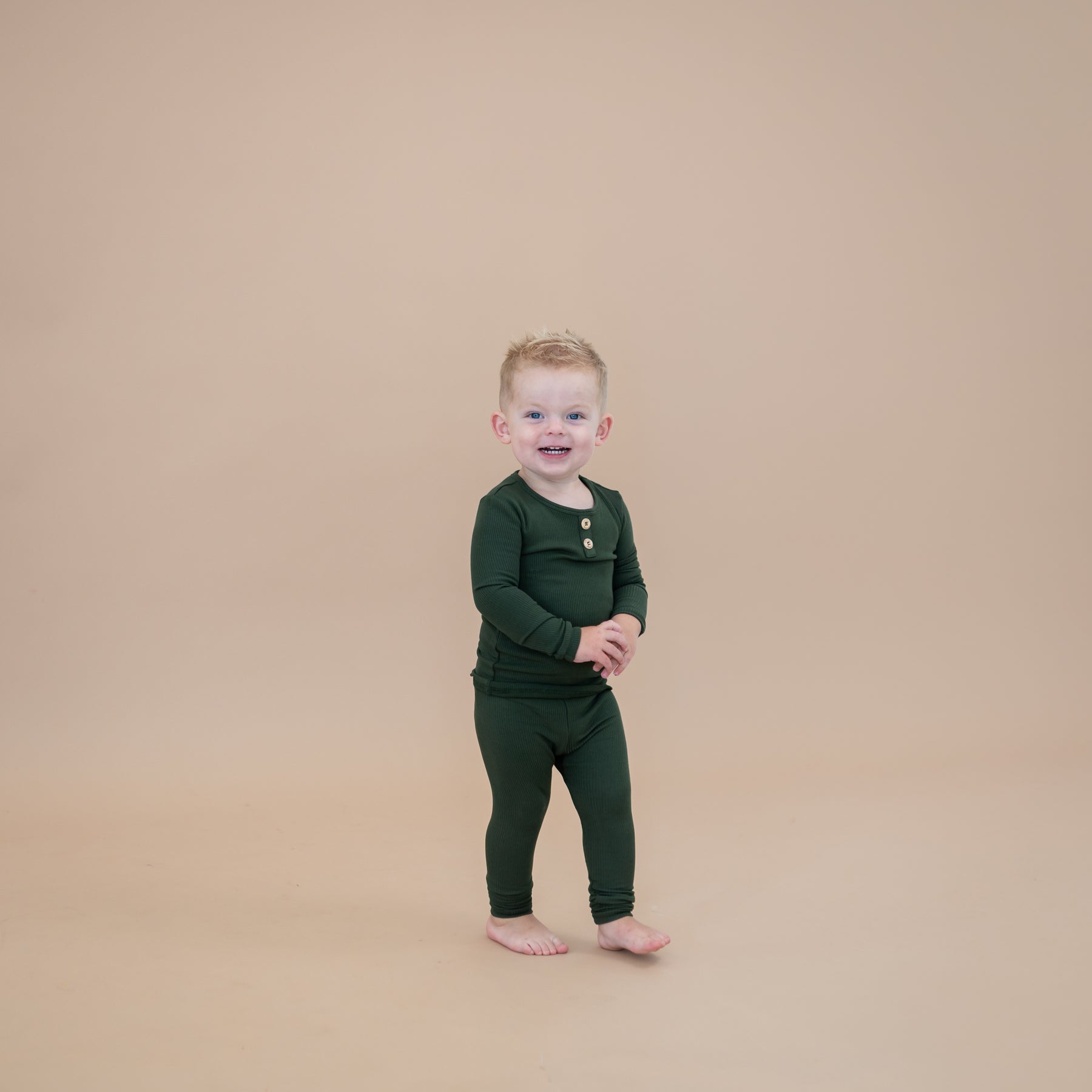 Toddler walking wearing the Ribbed Henley Set in Fir in front of a taupe colored backdrop