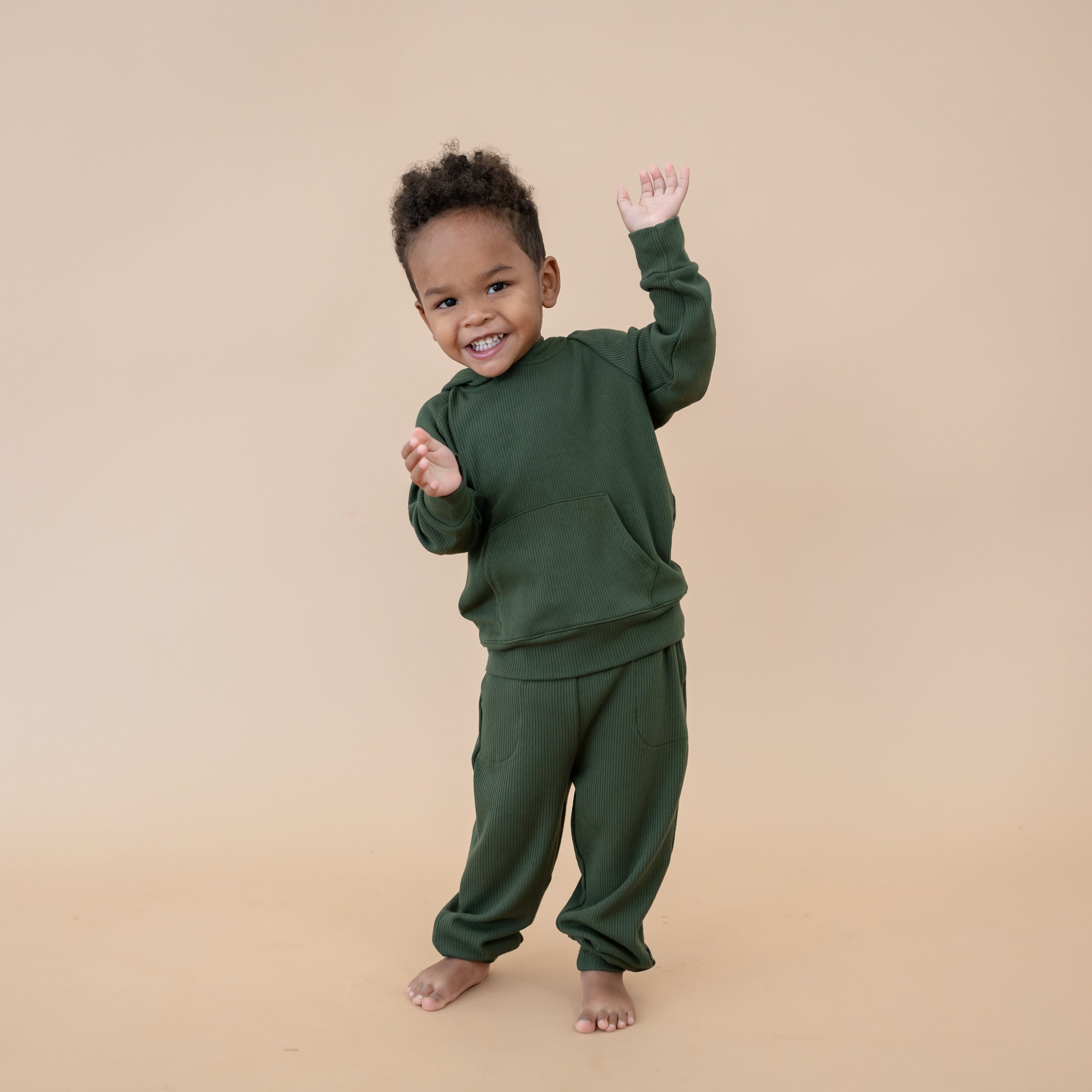 Young boy dancing wearing the Ribbed Hoodie in Fir and matching ribbed jogger pant in front of a taupe colored backdrop