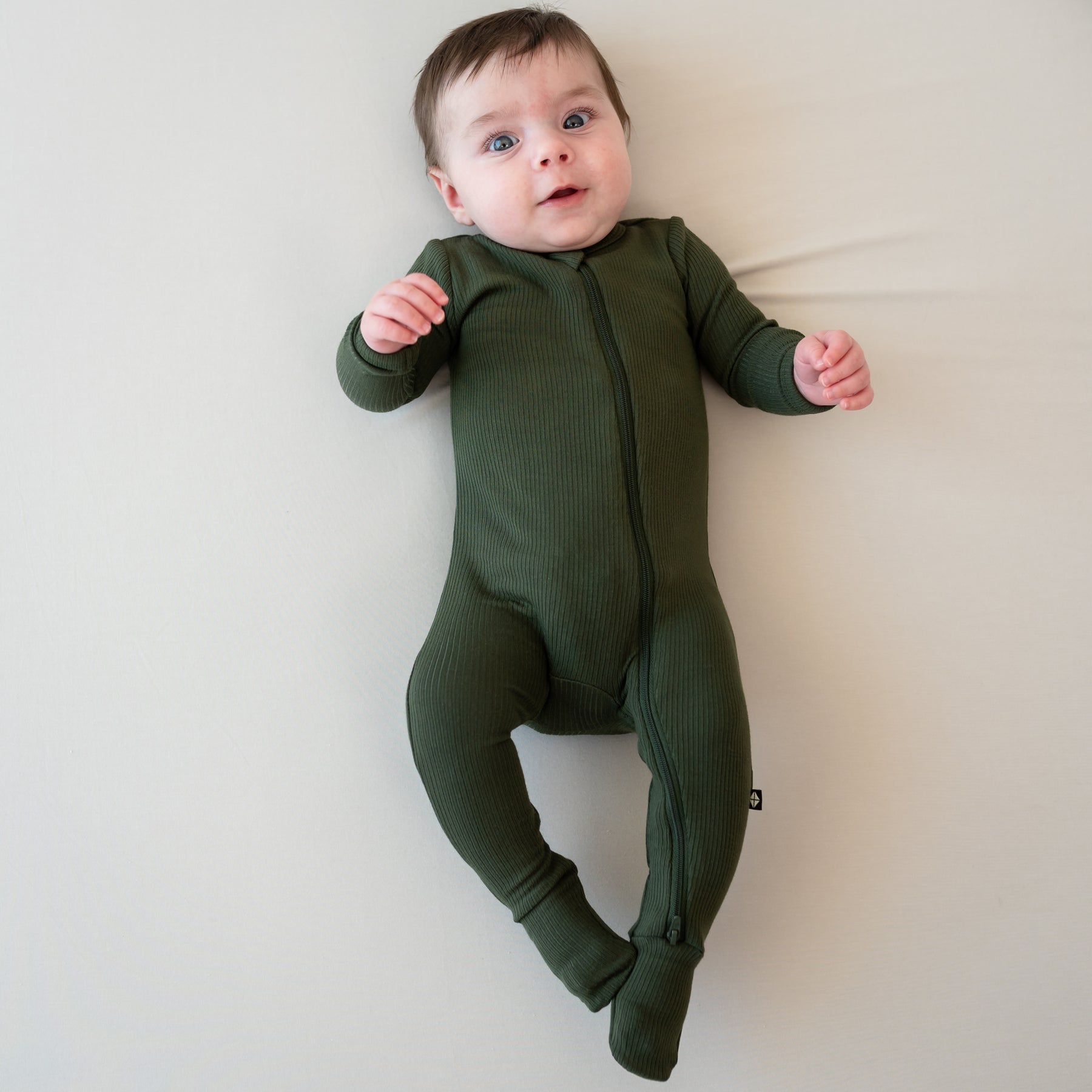 Infant laying on a Bisque blanket wearing the Ribbed Zipper Footie in Fir