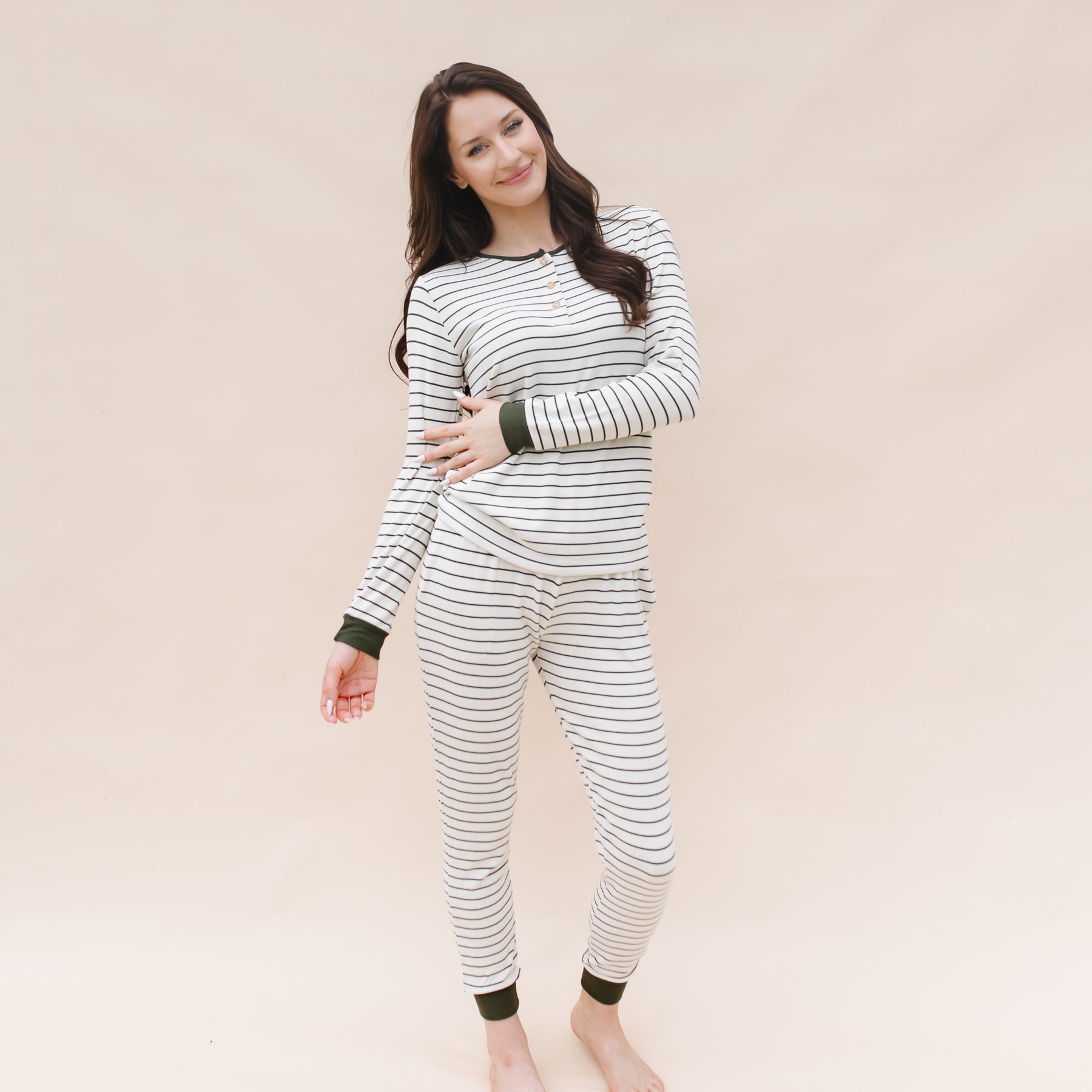 Smiling female model standing in front of a light beige background wearing the Women’s Ribbed Henley Set in Fir Stripe