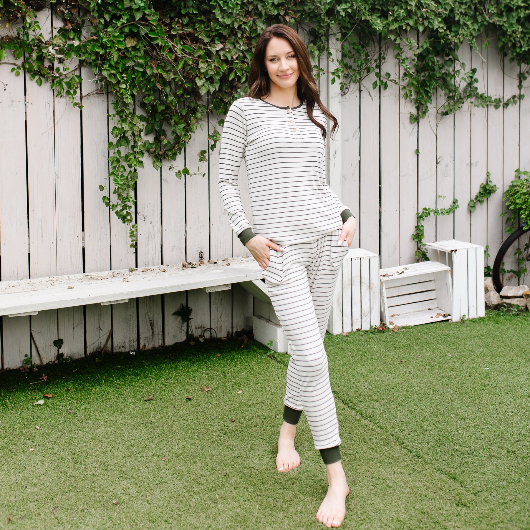 Female model standing in the grass in front of a white fence wearing the Women’s Ribbed Henley Set in Fir Stripe