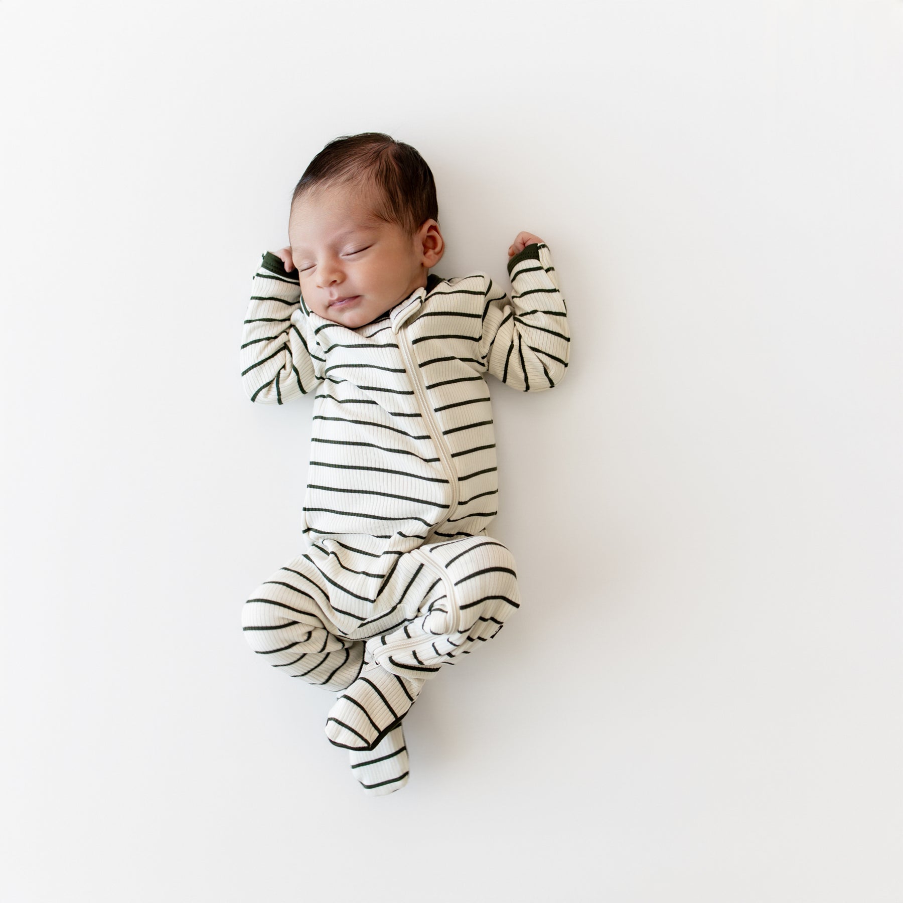 Sleeping newborn laying on a cream blanket wearing the Ribbed Zipper Footie in Fir Stripe