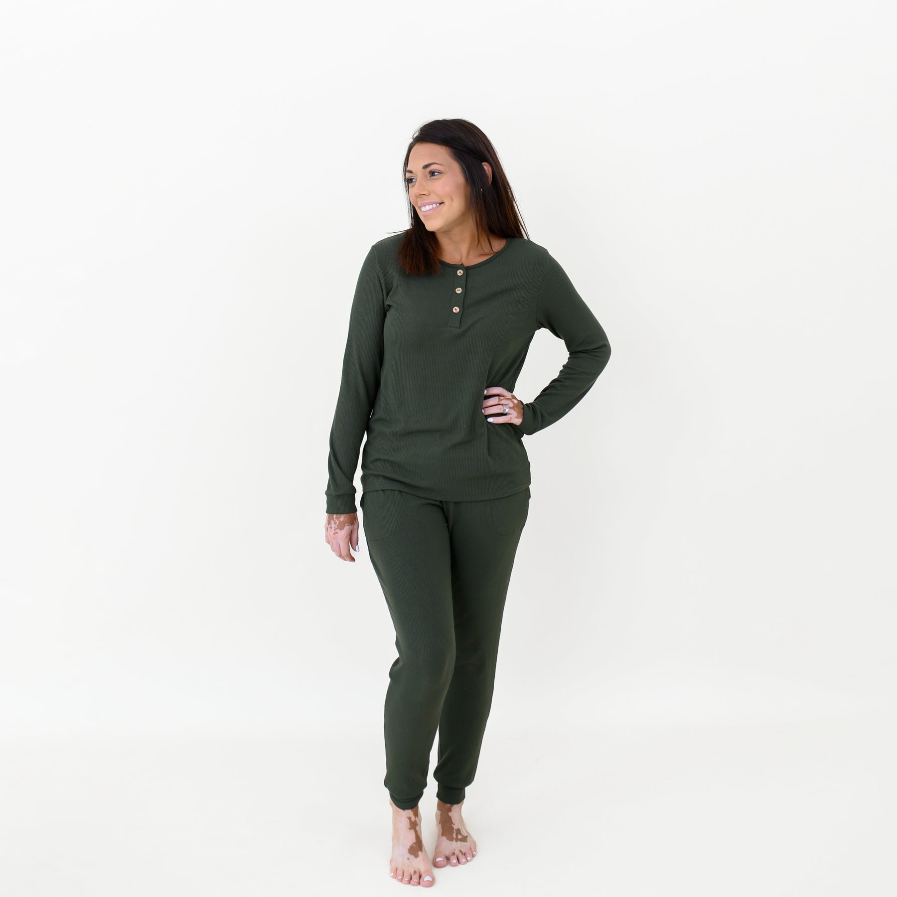 Female model standing with one hand on her hip wearing the Women’s Ribbed Henley Set in Fir in front of a white backdrop