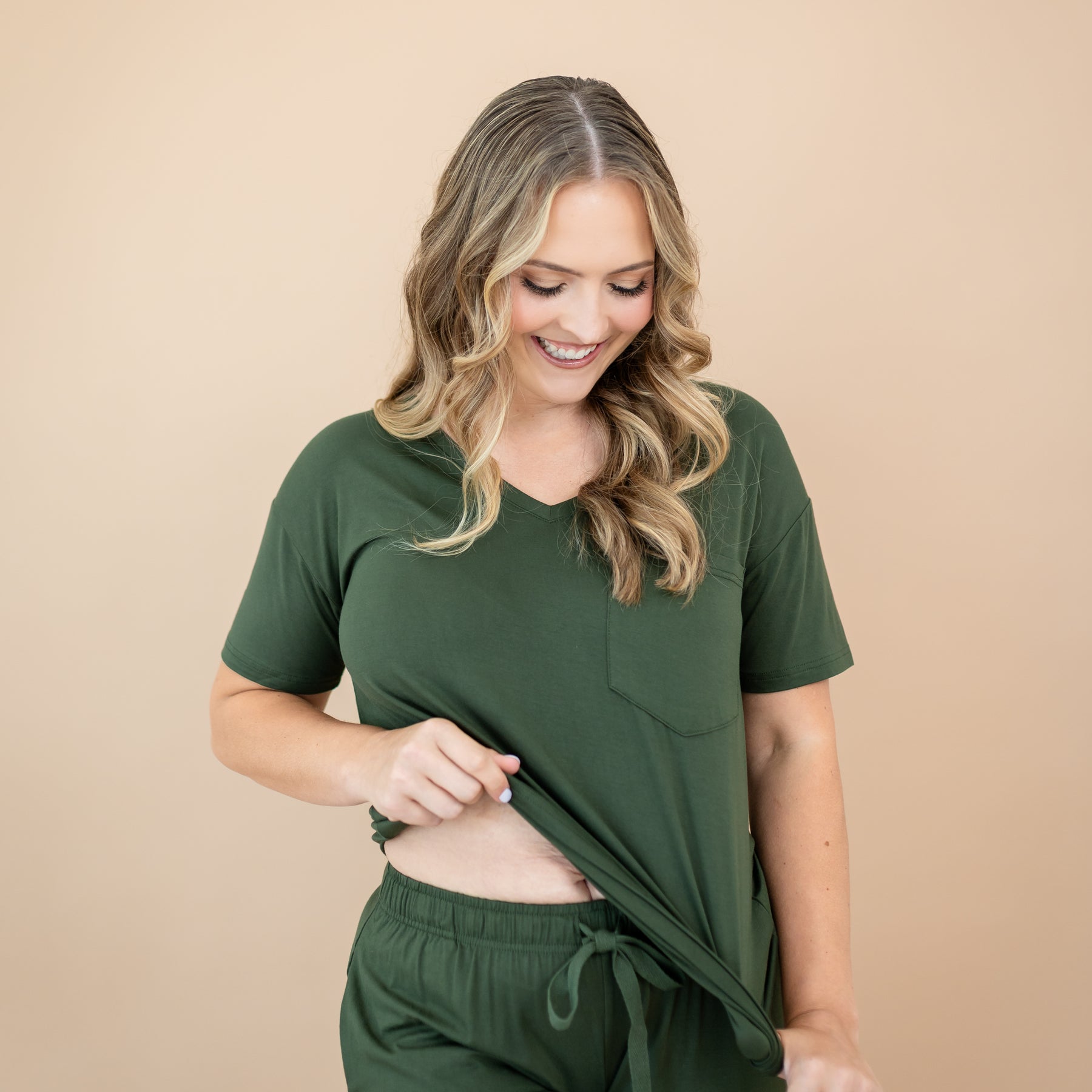 Woman wearing the Kyte Baby Women’s Relaxed Fit V-Neck in Fir against a beige background