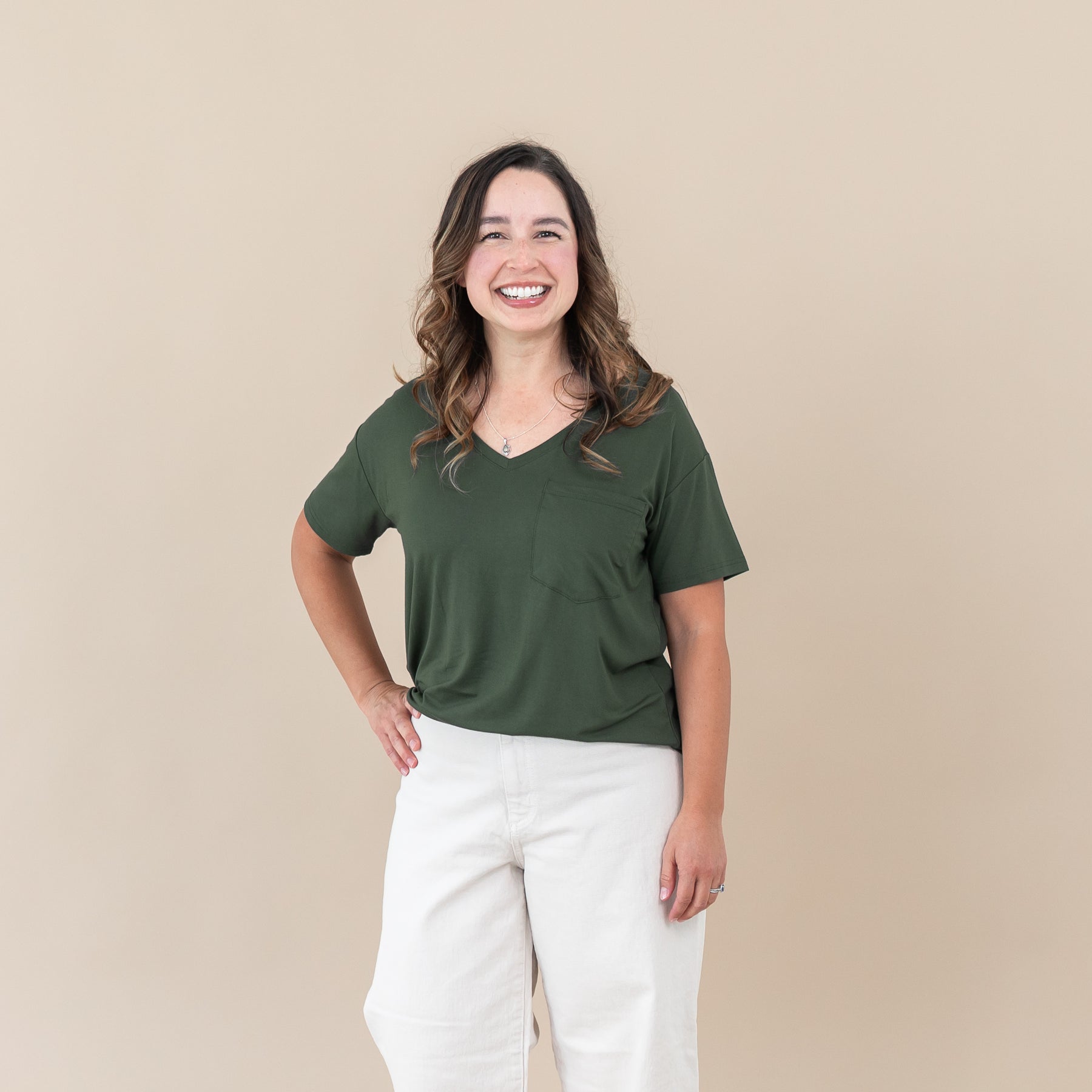 Woman wearing Women’s Relaxed Fit V-Neck in Fir and white pants against a beige background