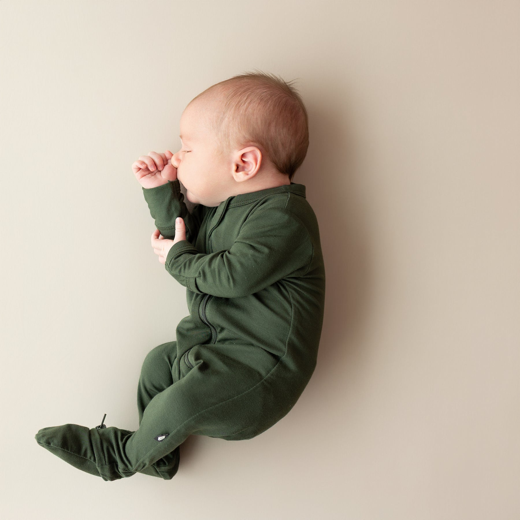 Baby in a green onesie lying on a beige surface