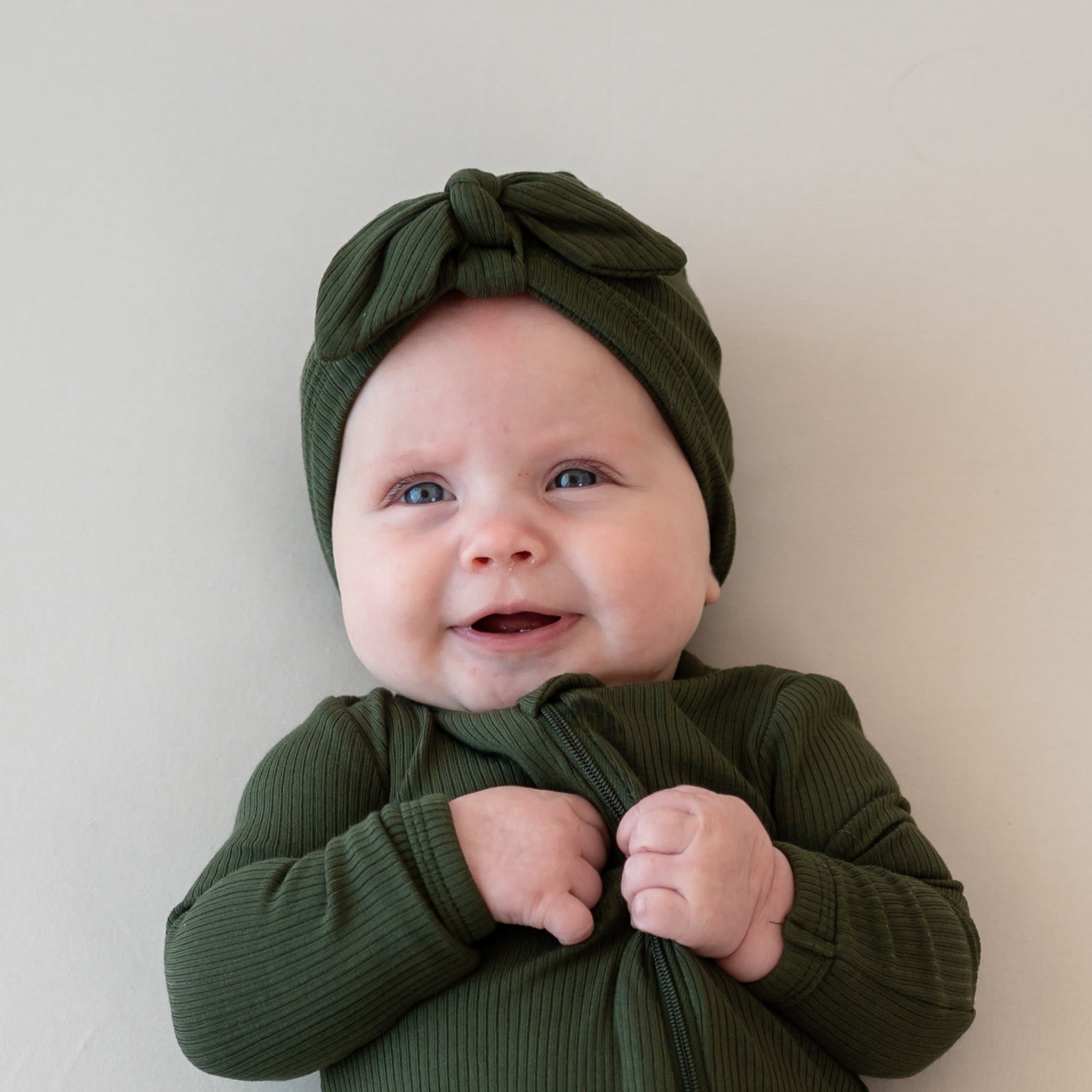 Close up of infant wearing the Ribbed Headwrap in Fir on a light neutral backdrop