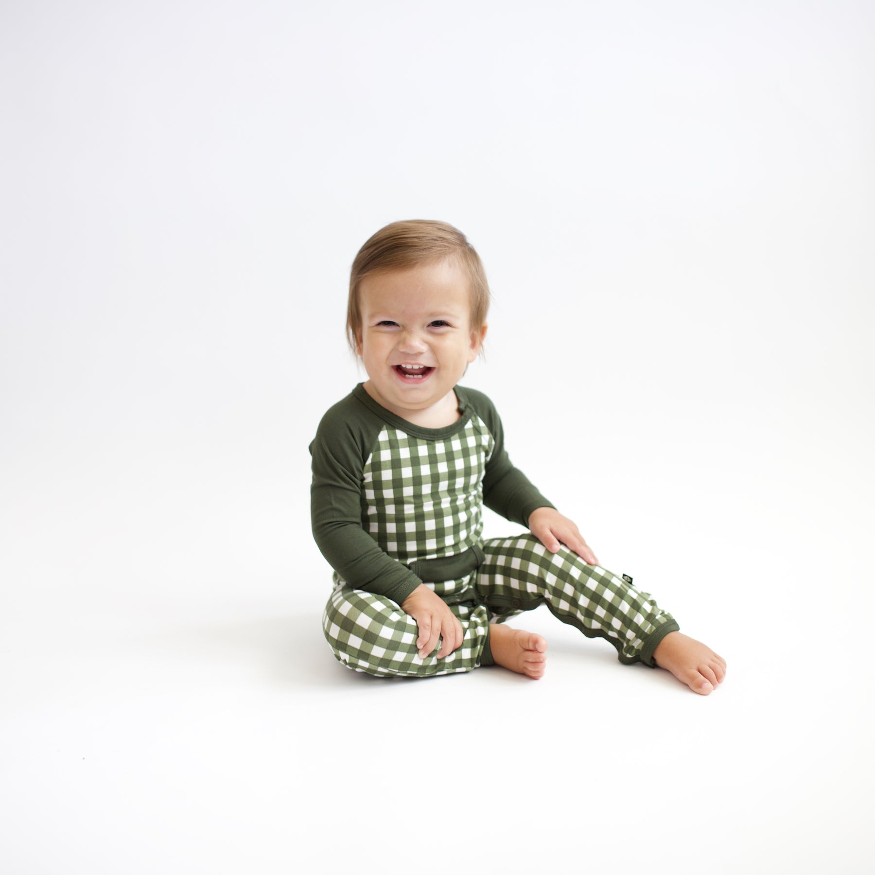 Young smiling toddler sitting wearing the Longall in Gingham Fir