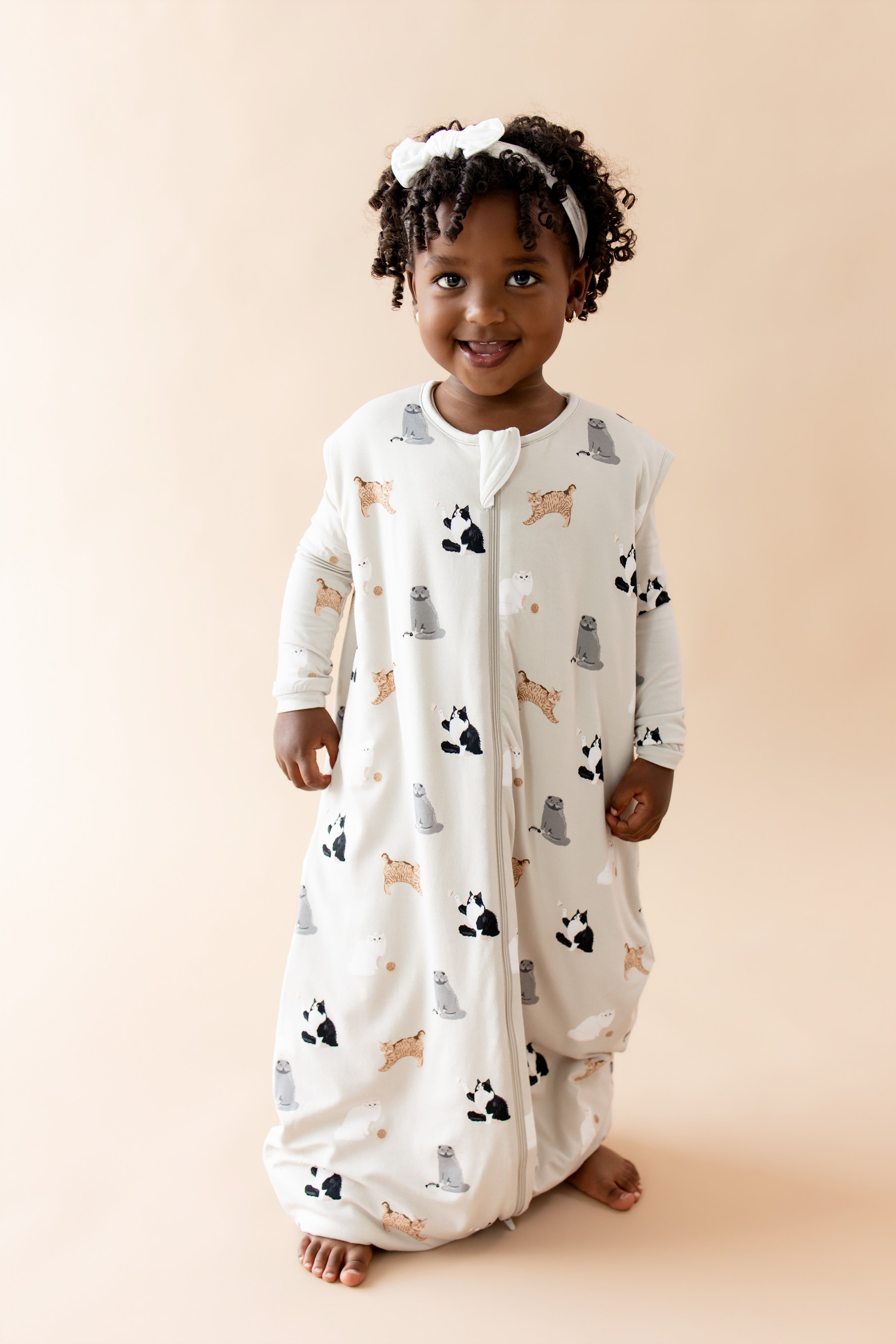 Child wearing a patterned sleep bag walker with cat designs on a beige background