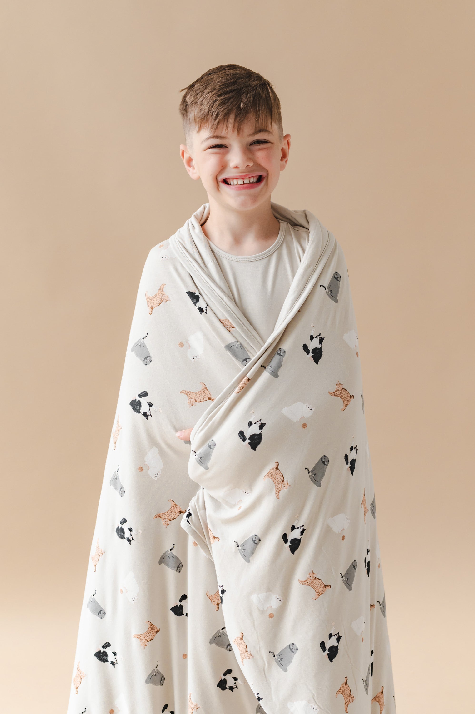 Child wrapped in a blanket with cat prints against a beige background