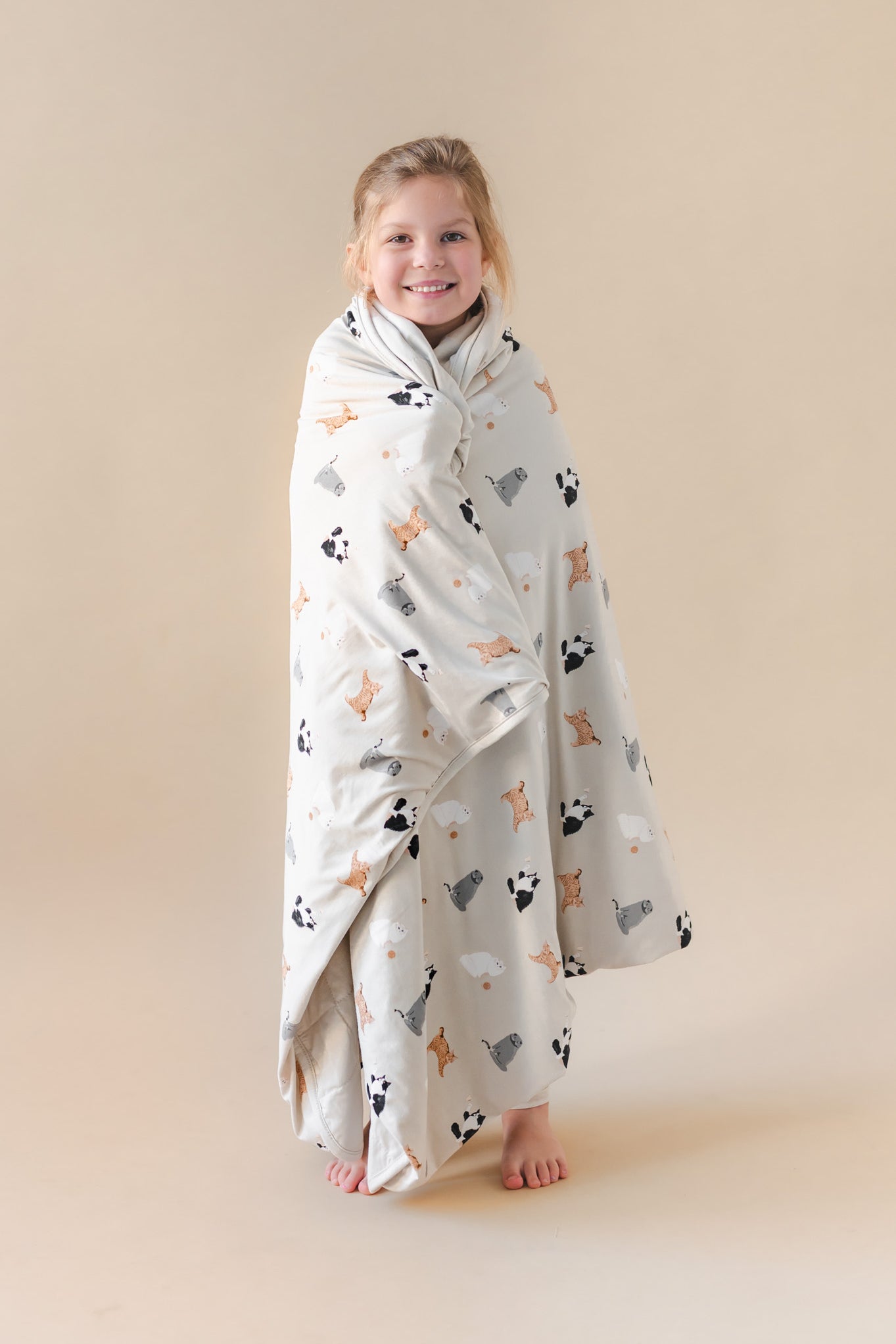 Child wrapped in a blanket with cat prints on a beige background