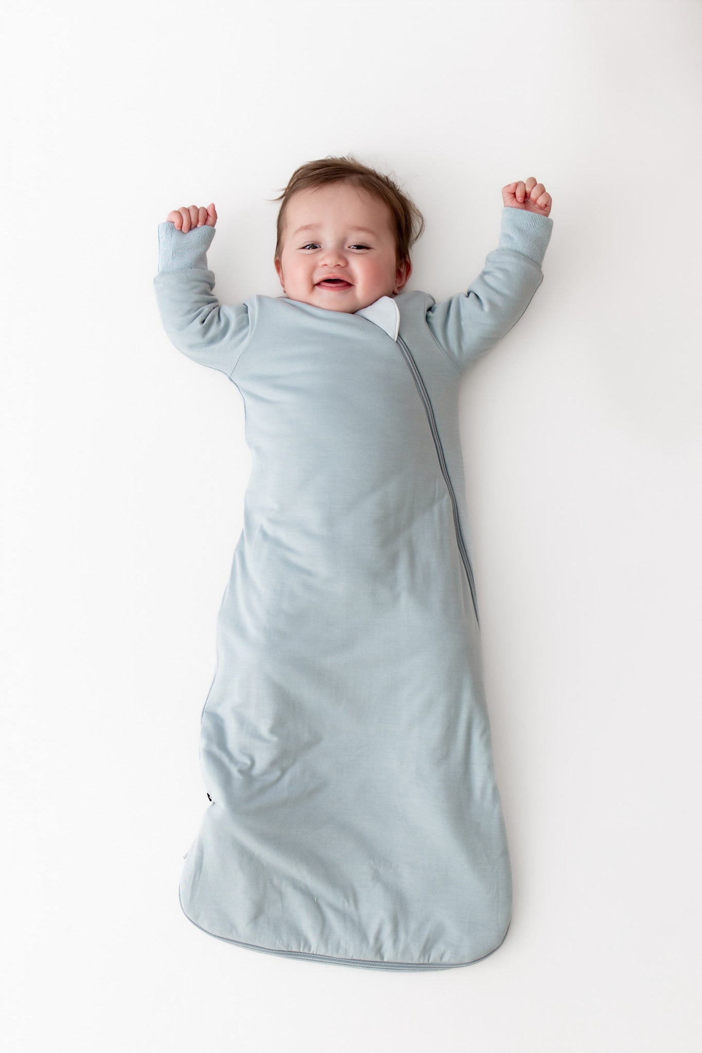 Baby wearing a long sleeve wearable blanket in a light blue color laying on a white surface