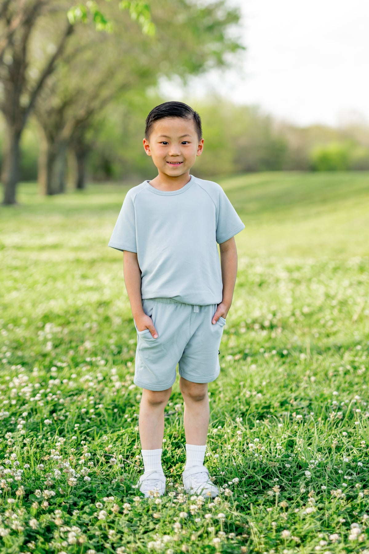 Young boy standing in a grass field wearing the Short Sleeve Jogger Set in Fog