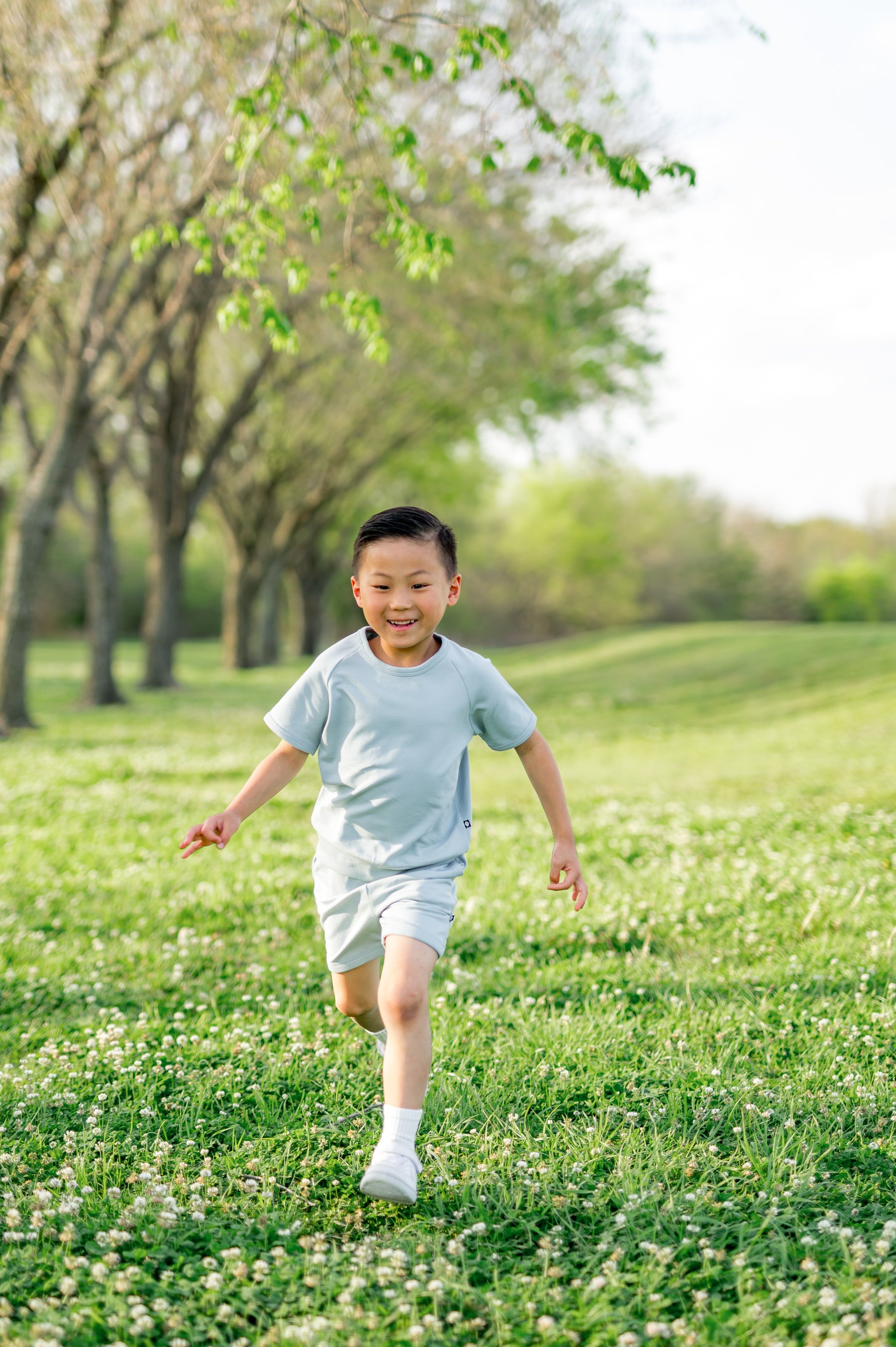 Young boy running through a grass field wearing the Short Sleeve Jogger Set in Fog
