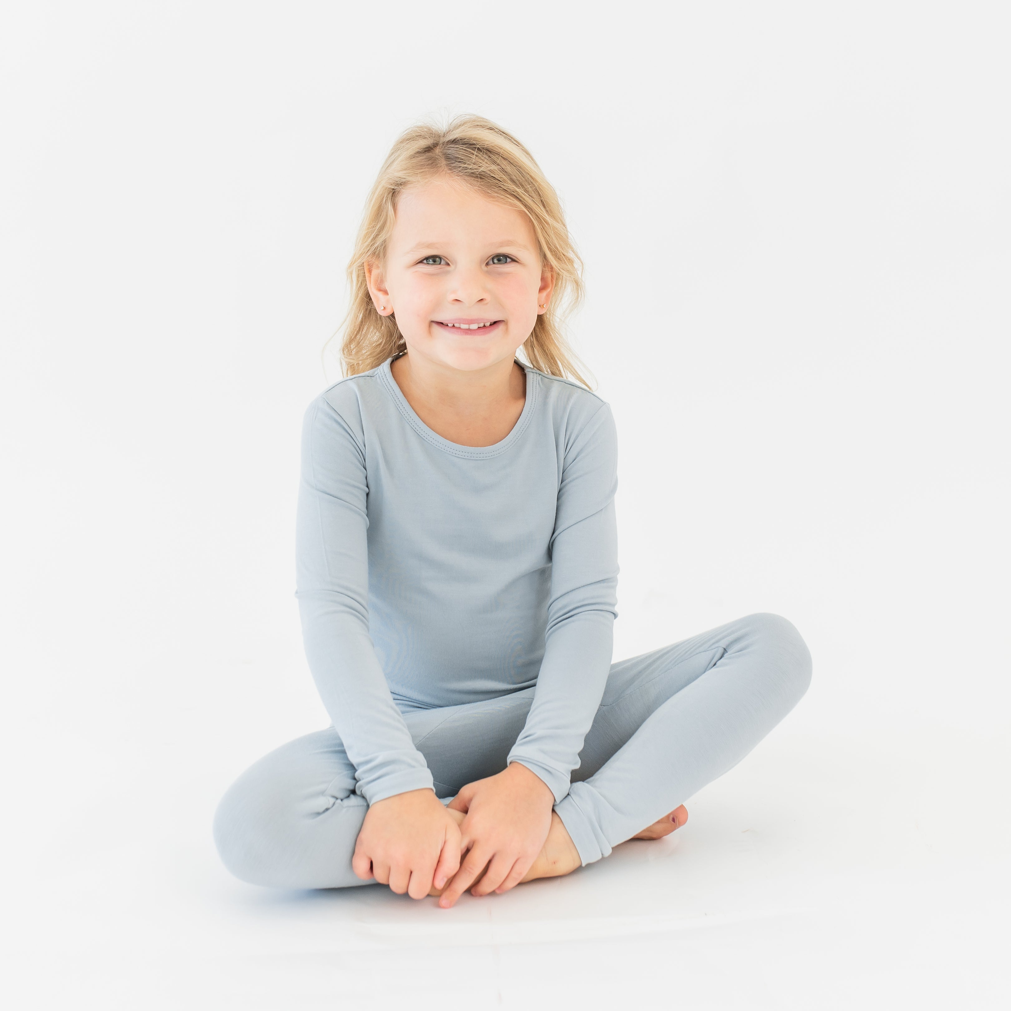 Young girl sitting on the floor cross legged wearing the Long Sleeve Pajamas in Fog 