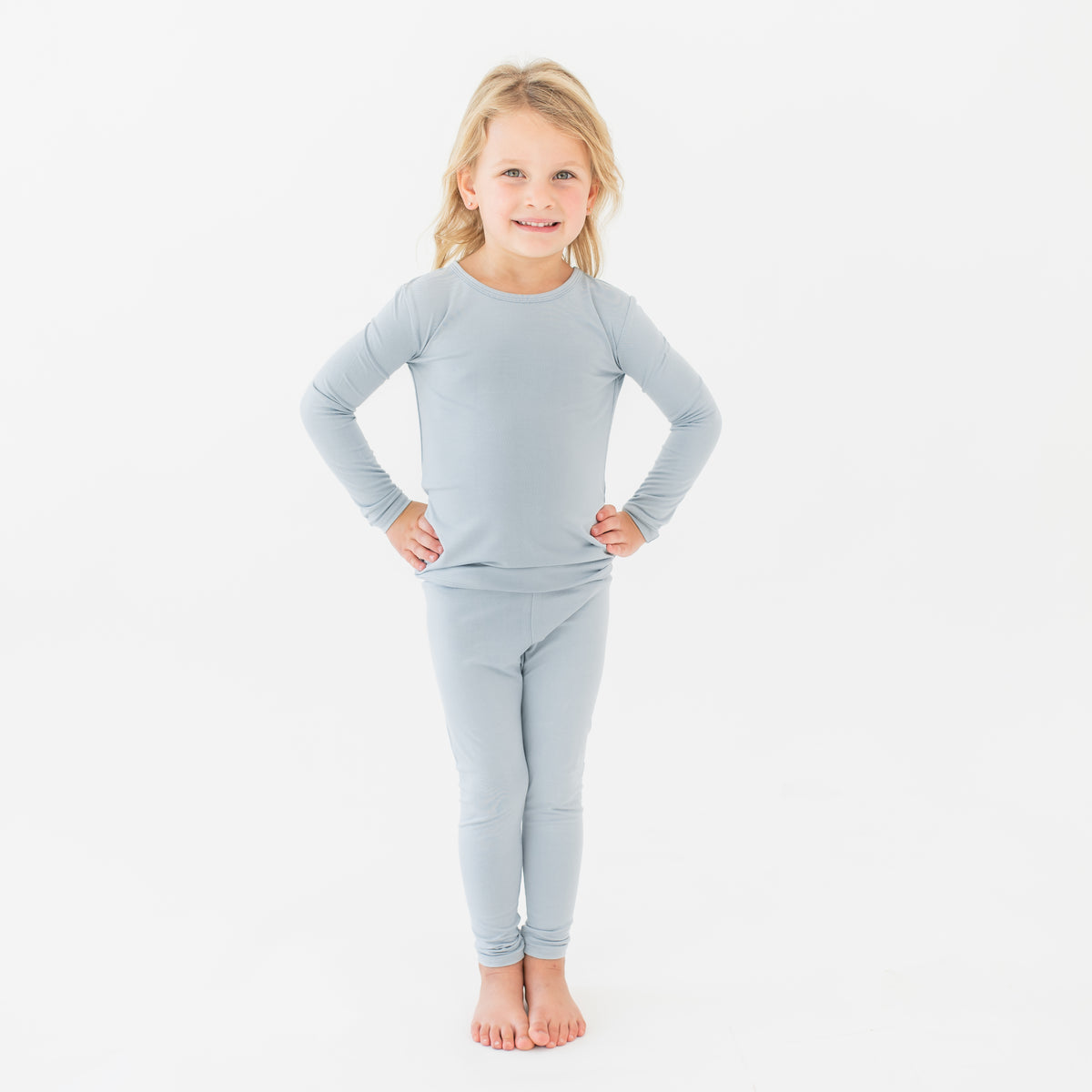 Young girl standing with both hands on her hips wearing the Long Sleeve Pajamas in Fog in front of a white background