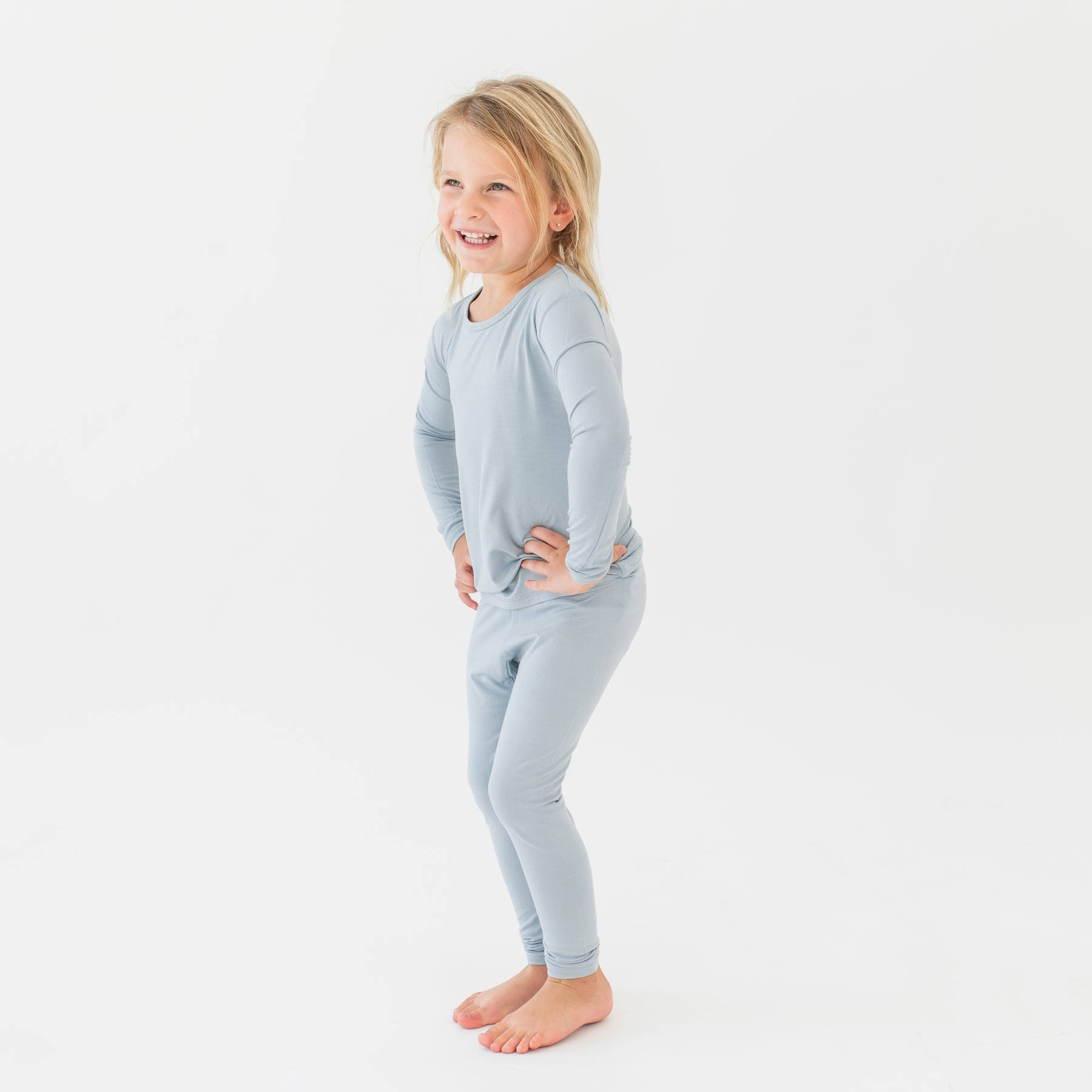 Young girl standing with her hands on her hips wearing the Long Sleeve Pajamas in Fog in front of a white background