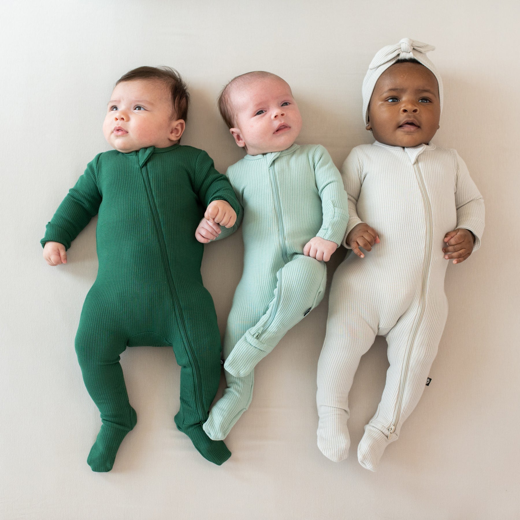 Babies wearing bamboo Kyte Baby Ribbed Zippered Footie pajamas in core colors