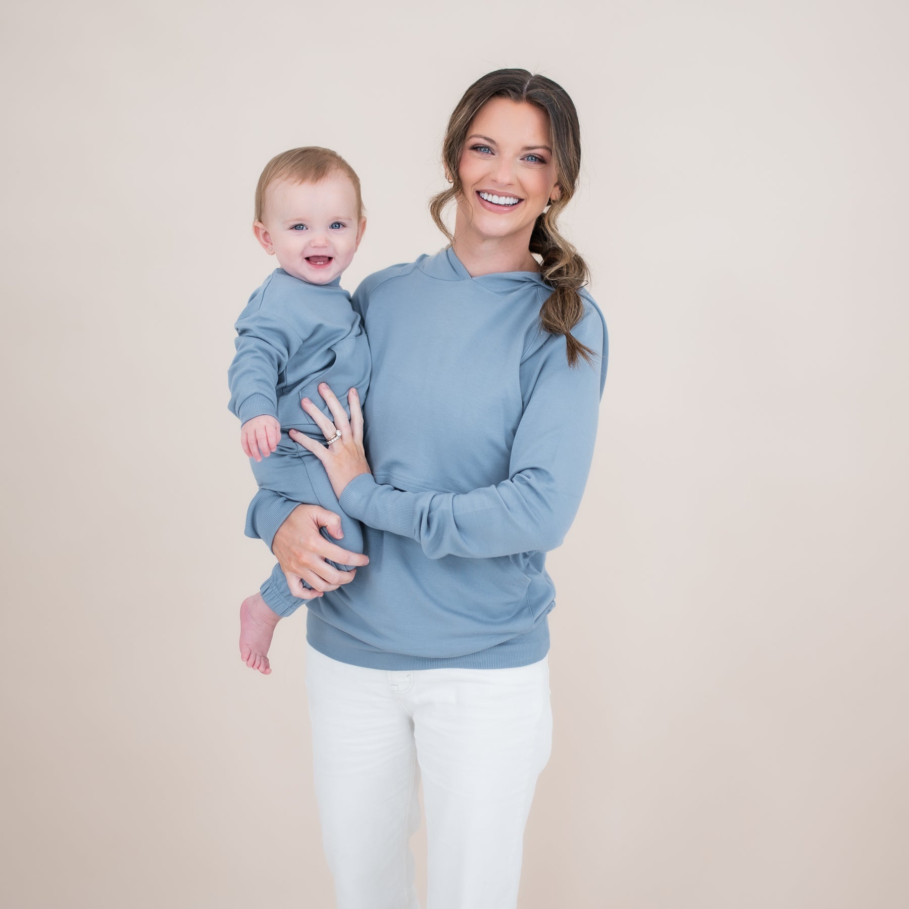 Mother wearing the Women's French Terry Nursing Hoodie in Slate and white pants holding her infant who is in a matching french terry jogger set
