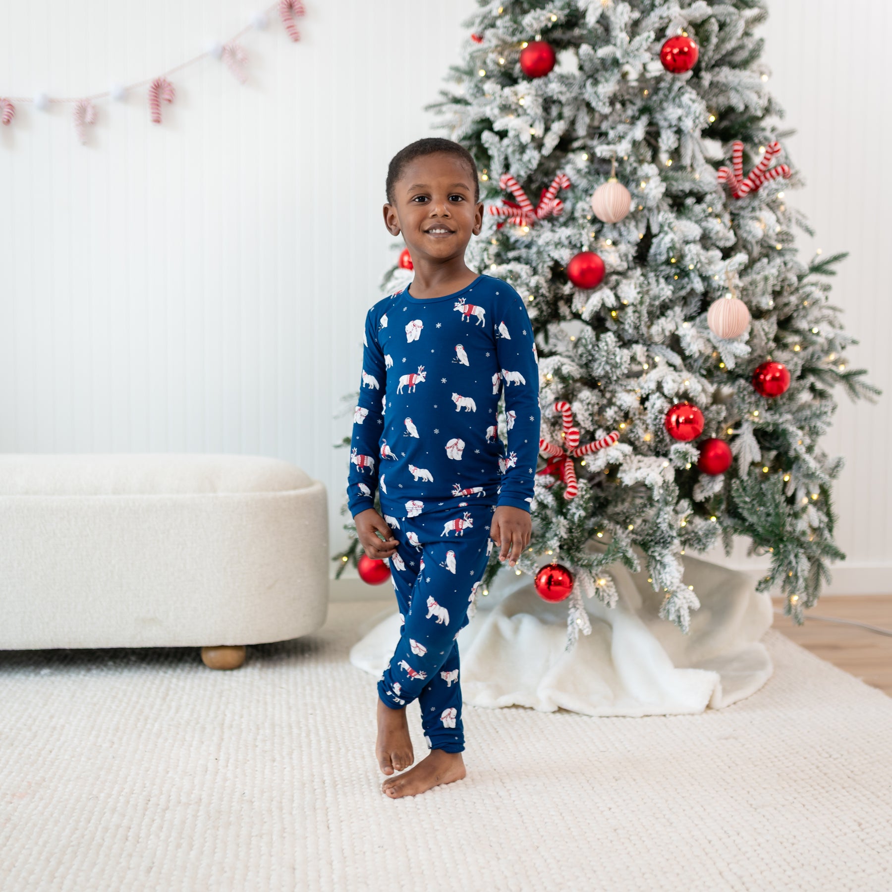 Young boy standing in front of a decorated Christmas tree wearing the Long Sleeve Pajamas in Frosty Friends